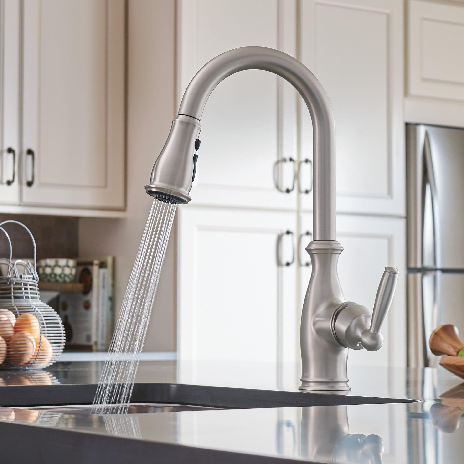 Brushed stainless steel kitchen faucet with curved spout and pull-down sprayer head over dark countertop.