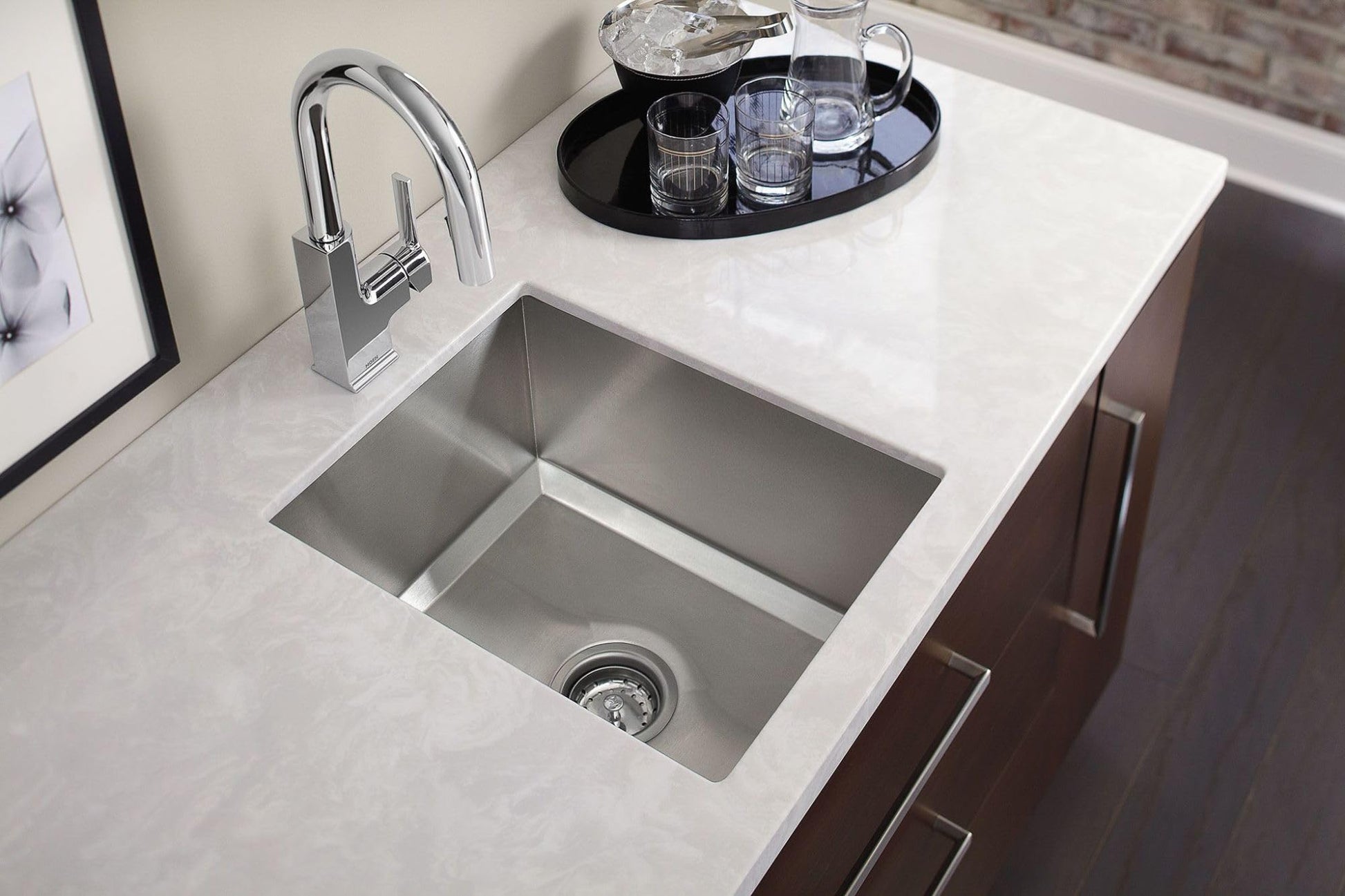 Stainless steel undermount sink with single bowl installed in white countertop next to chrome faucet.