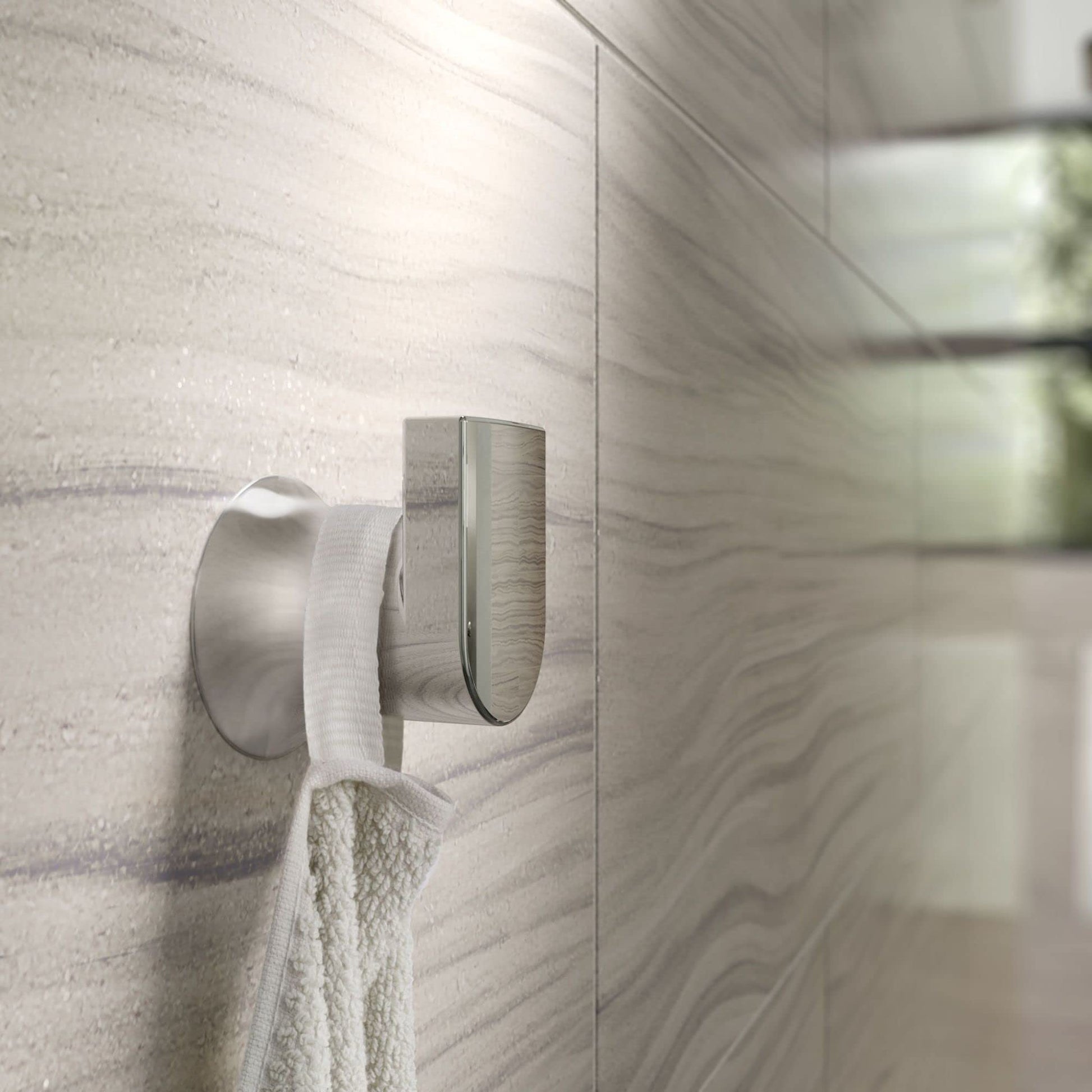 Chrome wall-mount robe hook with curved arm holding a white towel on marble tile wall.