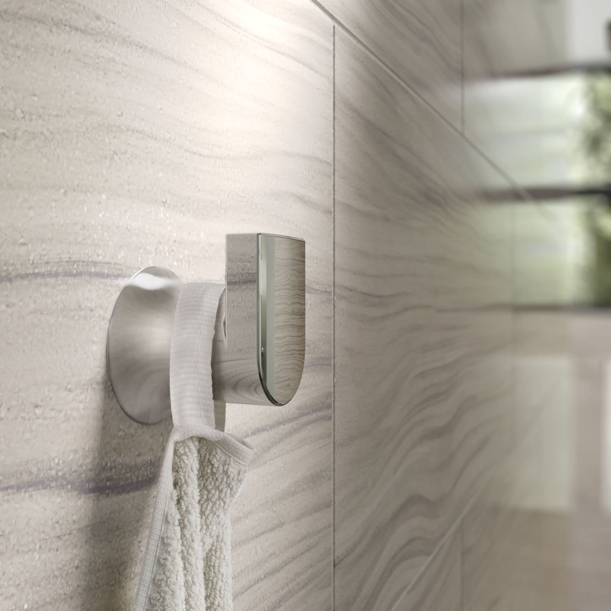 Chrome wall-mount robe hook with curved arm holding a white towel on marble tile wall.