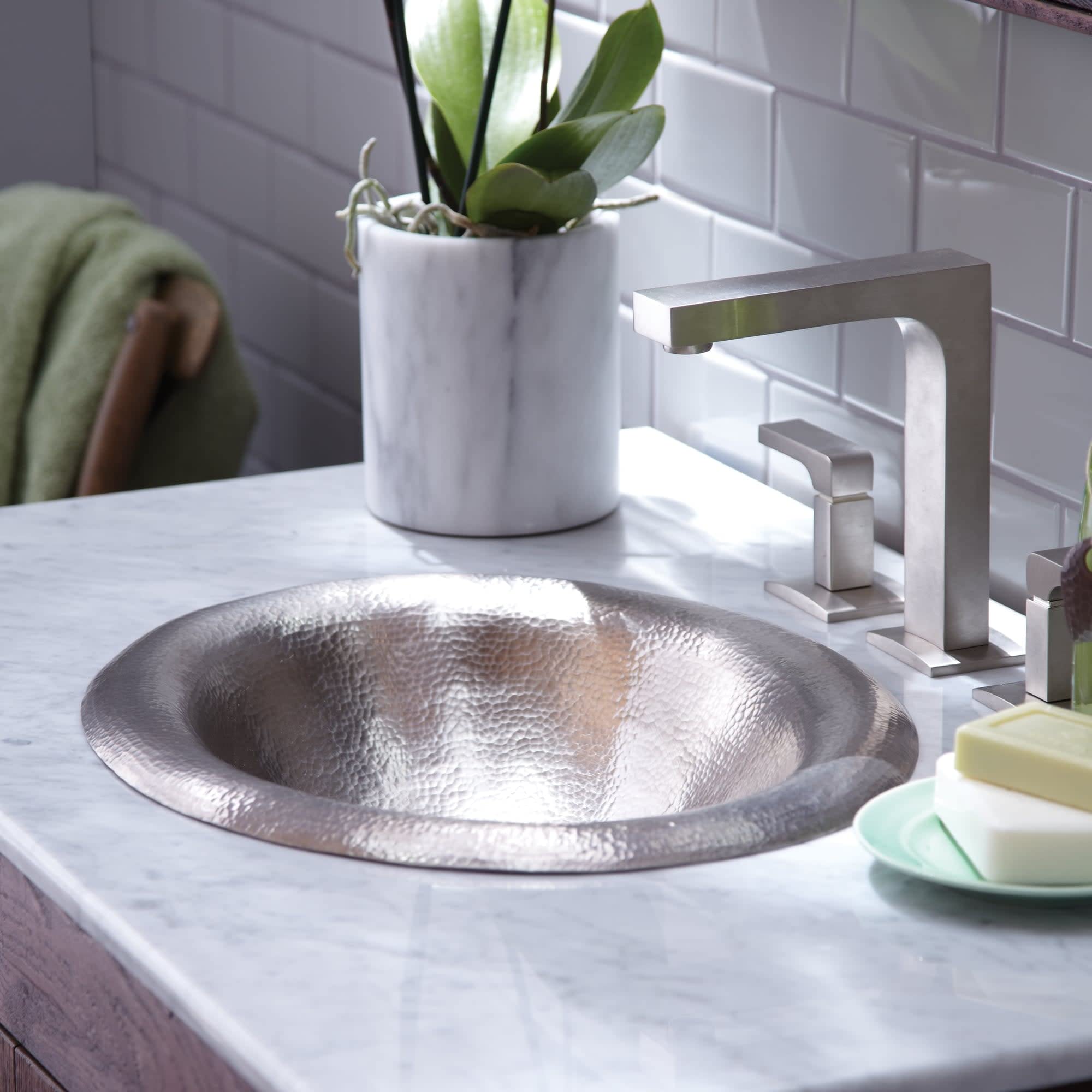 Hammered copper sink with lotus-petal edges on marble countertop with brushed nickel faucet.