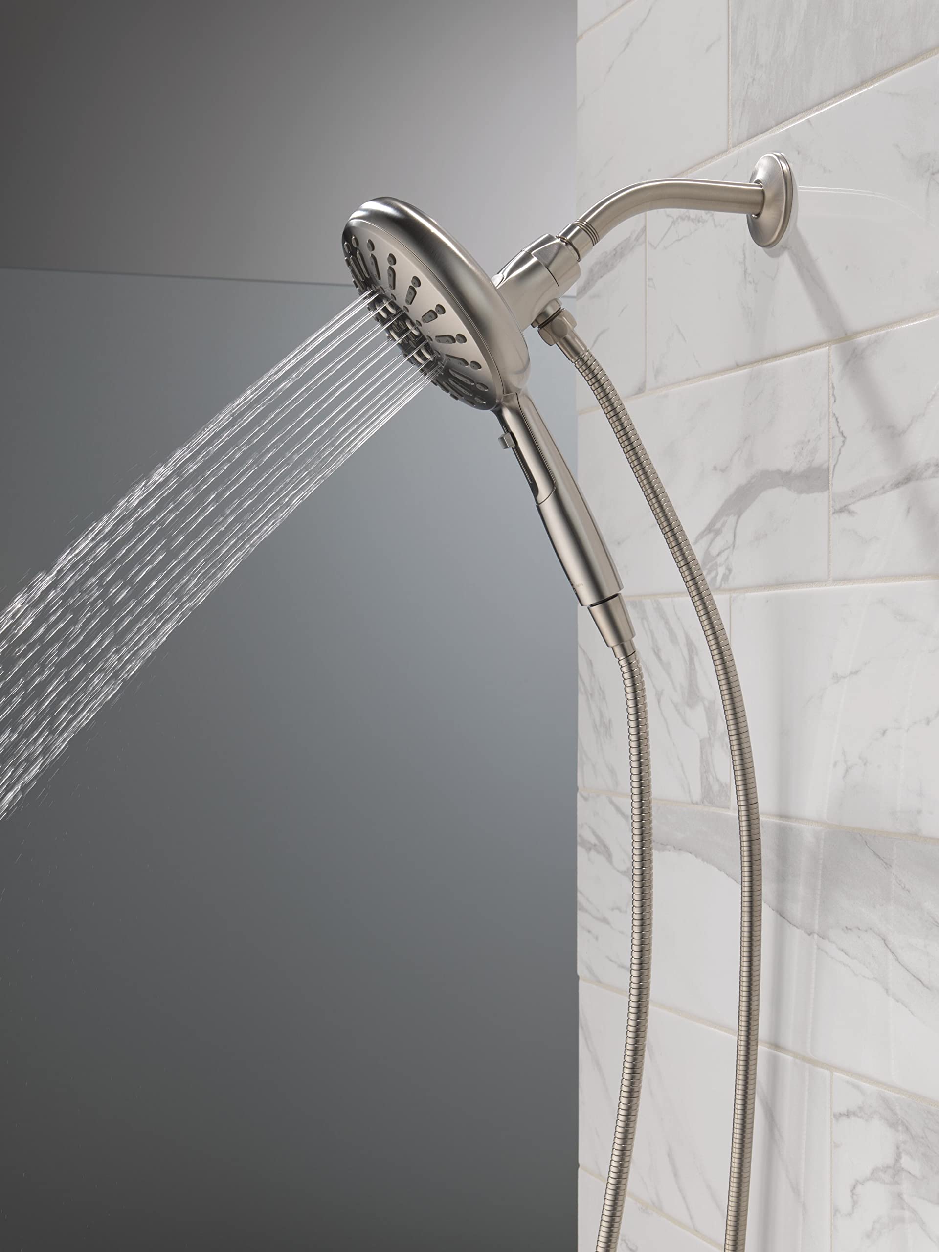 Stainless steel hand shower with multiple spray settings and flexible hose attached to wall mount on marble tile.