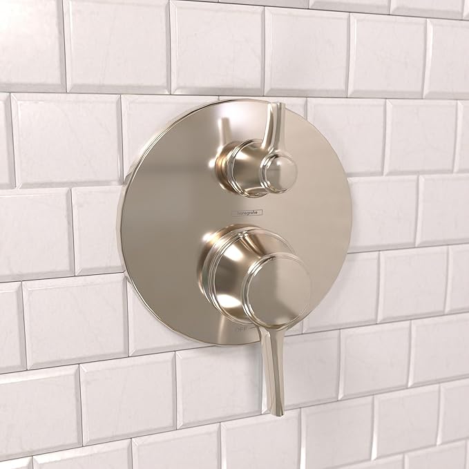 Round polished nickel shower valve trim with two metal handles and diverter on white subway tile.