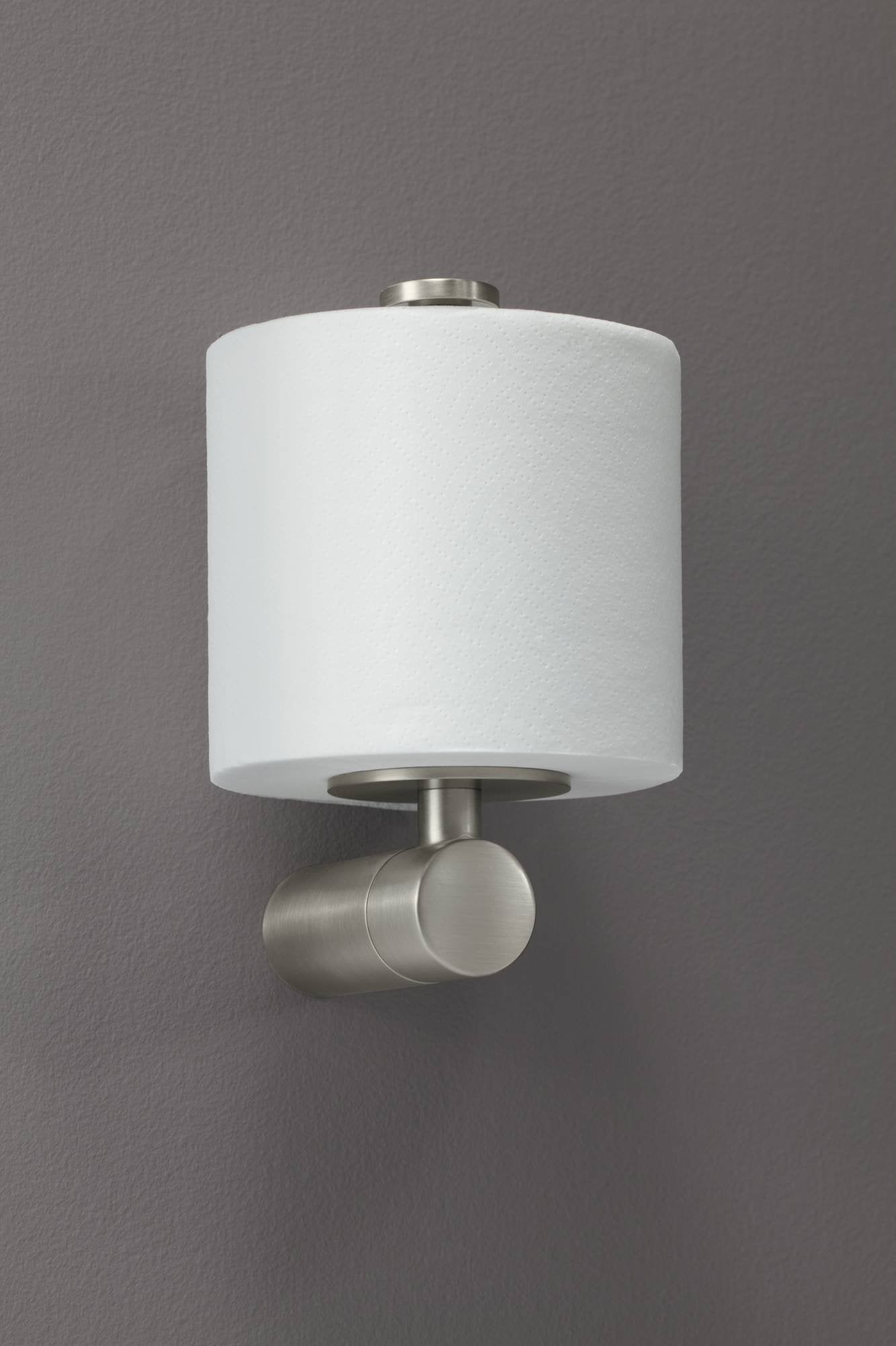 Brushed nickel toilet paper holder with cylindrical white roll and rounded knob on gray wall.