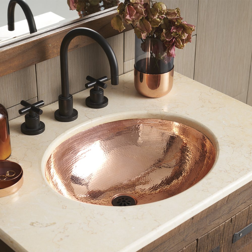 Polished copper oval sink with hammered texture installed in marble countertop, paired with black three-hole faucet.