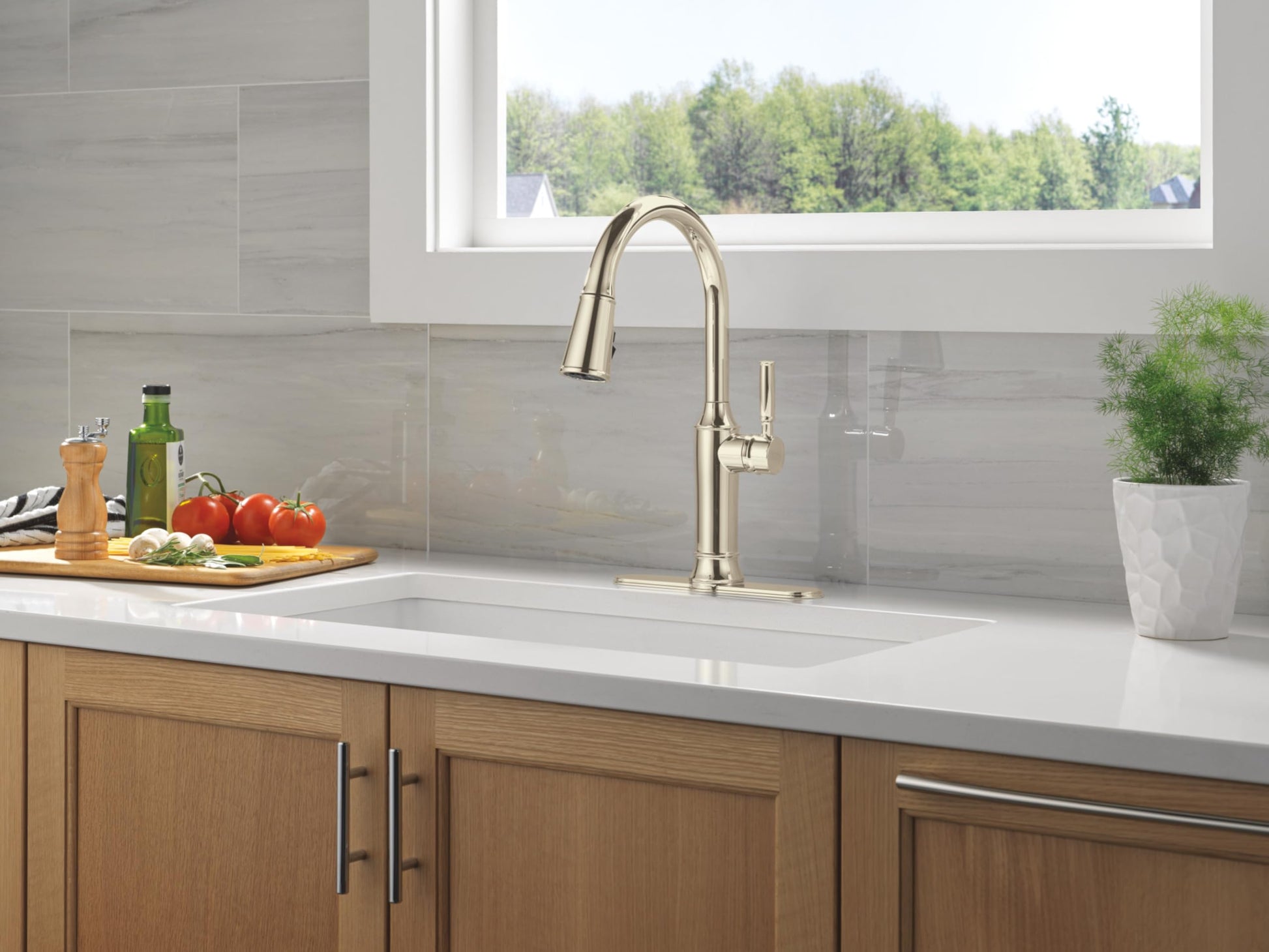 Stainless steel pull-down kitchen faucet with curved spout mounted on white countertop sink.