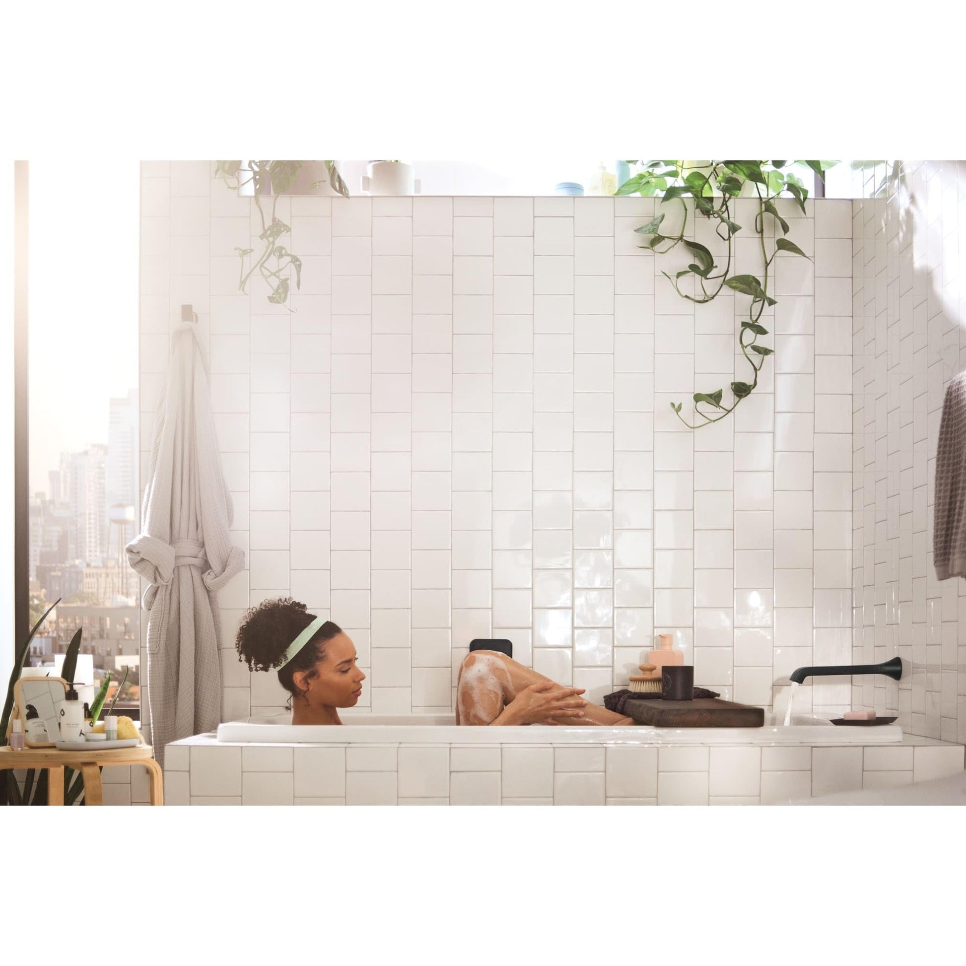Chrome wall-mounted tub faucet with single handle and curved spout installed above white tile bathtub surround.