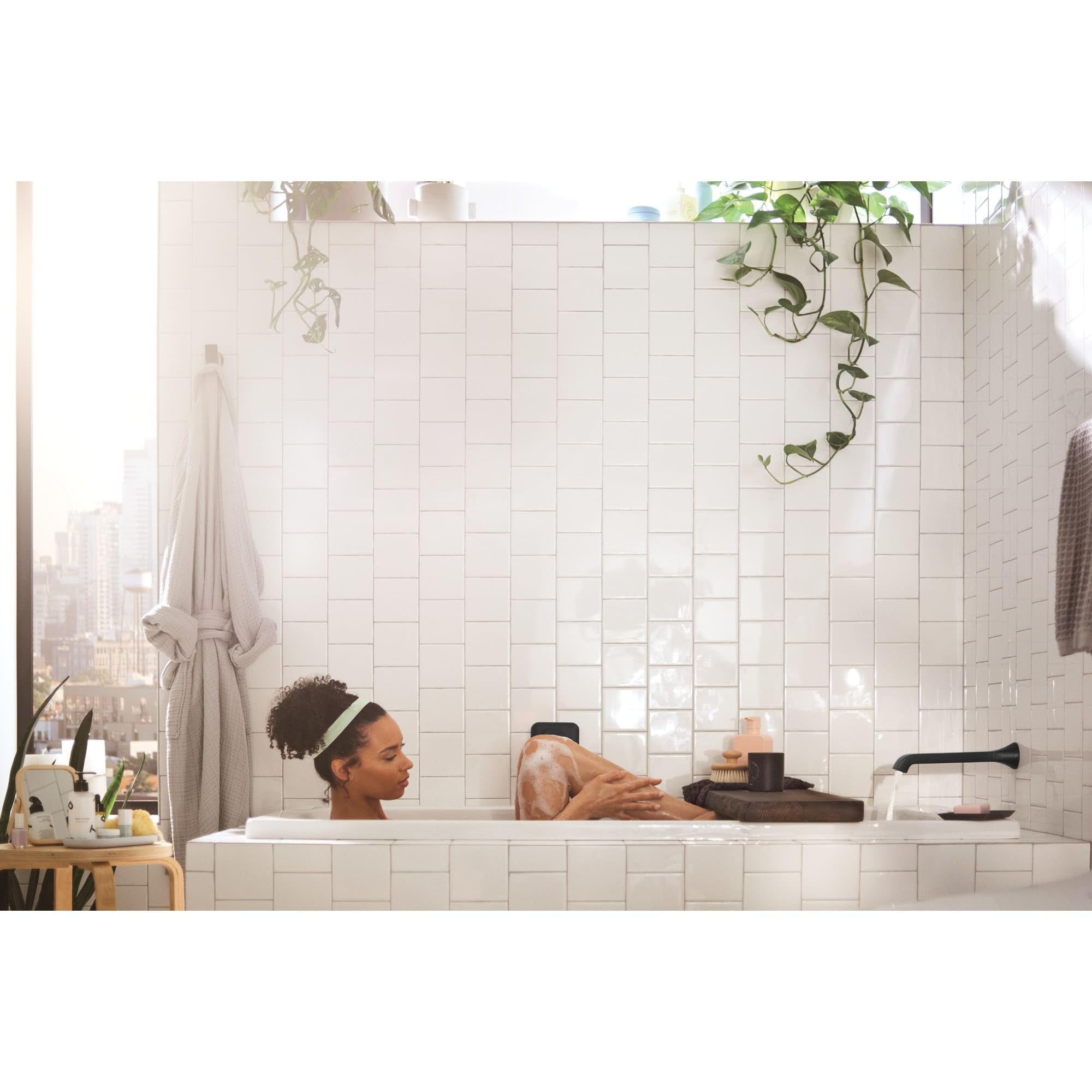 Chrome wall-mounted tub faucet with single handle and curved spout installed above white tile bathtub surround.