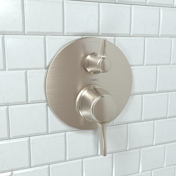 Round brushed nickel pressure balance valve trim with upper diverter lever and lower control knob mounted on white subway til