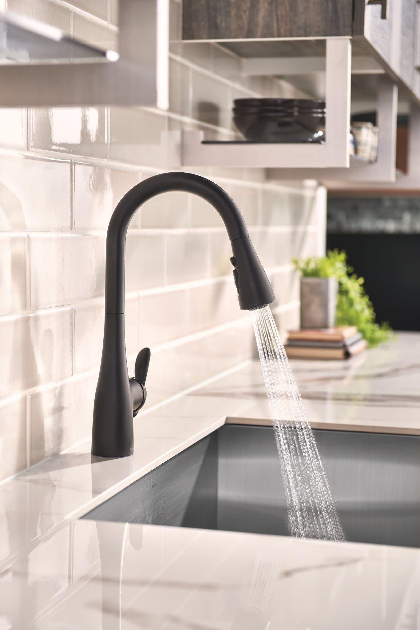 Matte black kitchen faucet with pulldown sprayer installed over undermount sink with white subway tile backsplash.
