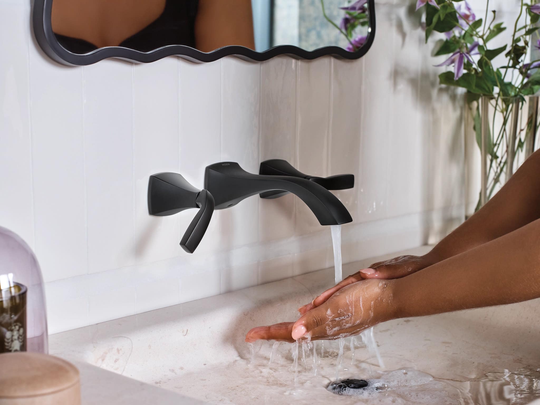 Matte black two-handle wall-mounted bathroom faucet with curved spout and lever handles installed above sink basin.