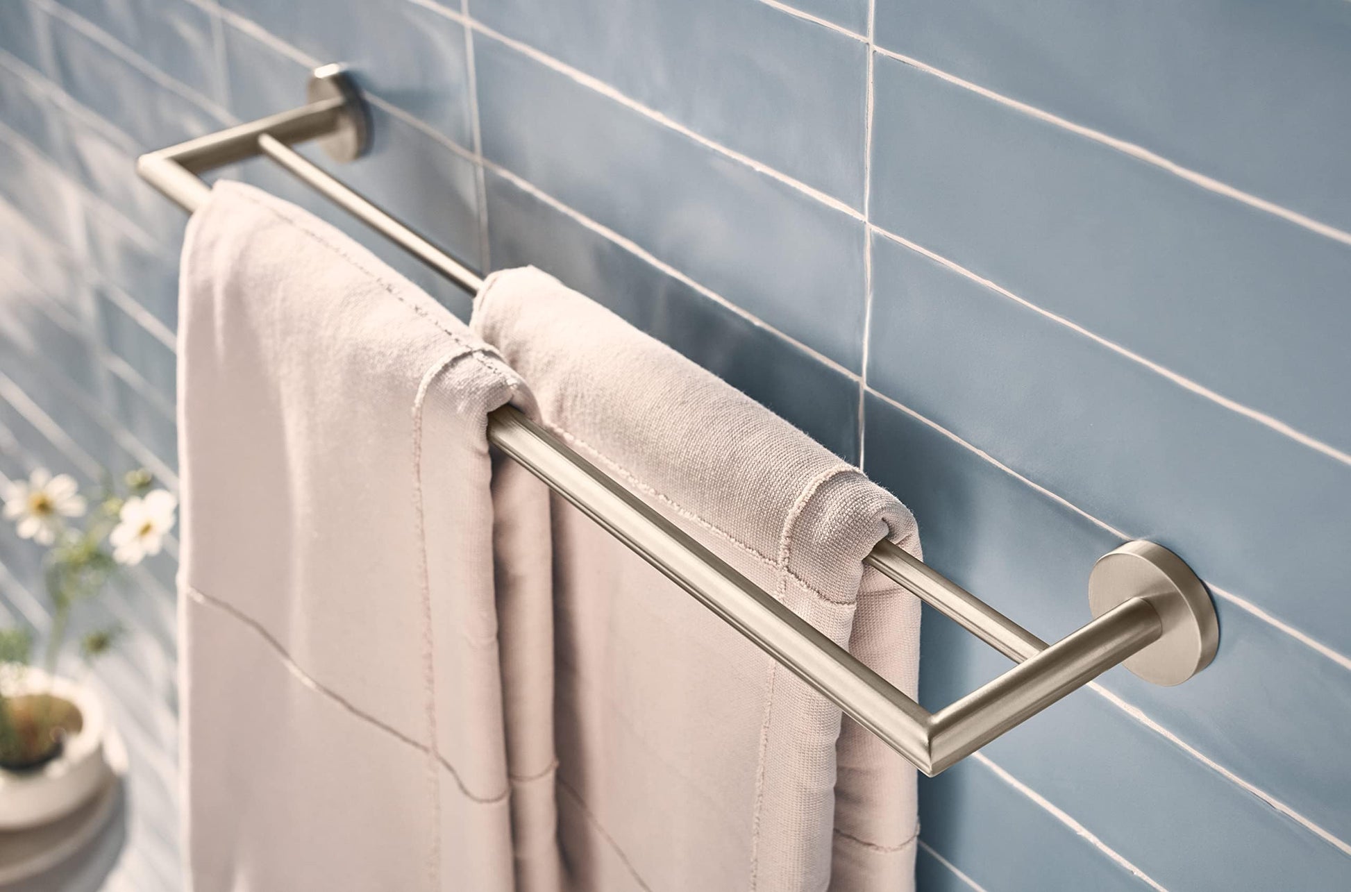 Brushed nickel double towel bar mounted on white subway tile wall with rolled towels draped over both bars.