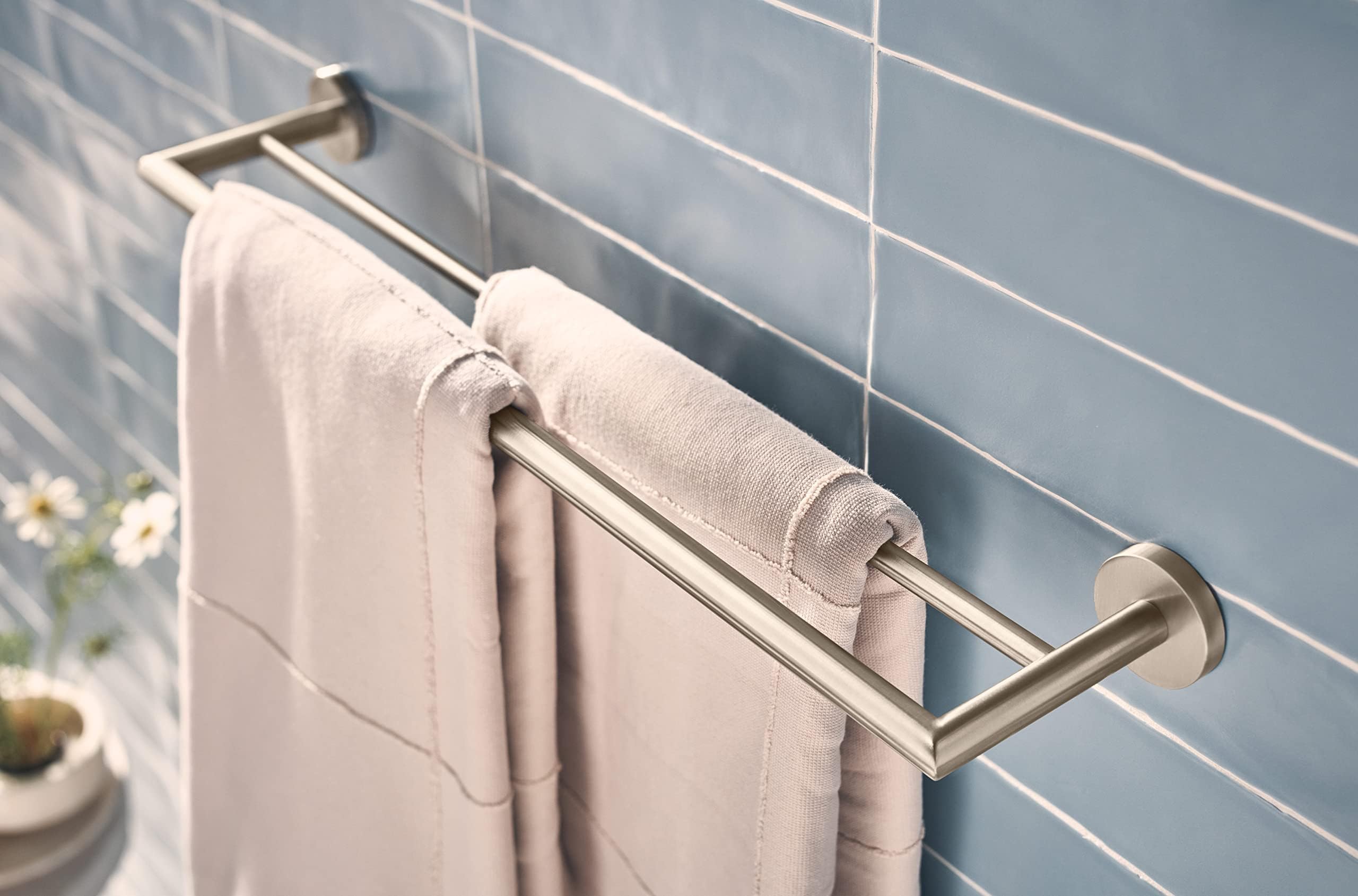 Brushed nickel double towel bar mounted on white subway tile wall with rolled towels draped over both bars.