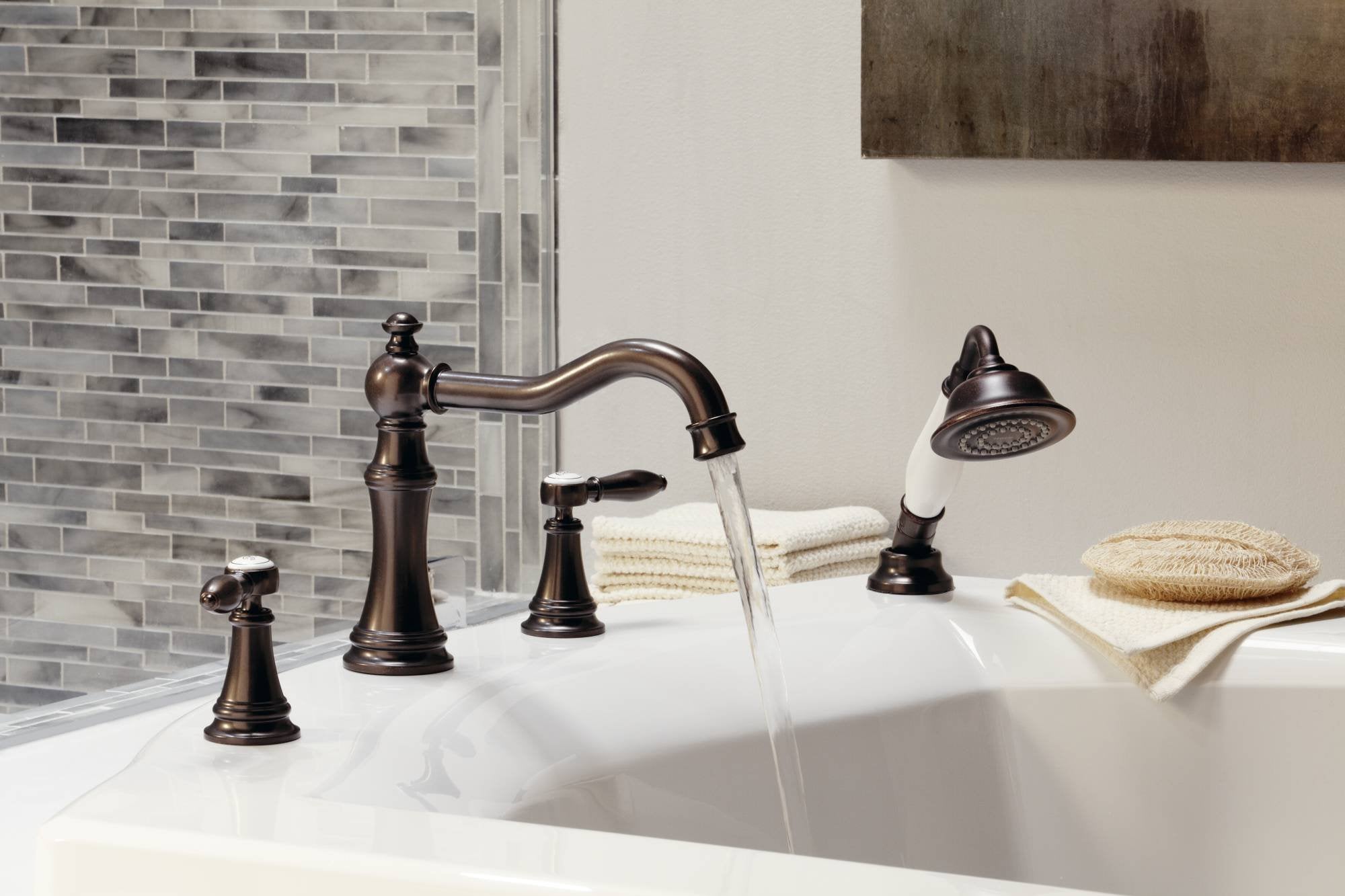 Chrome two-handle roman tub faucet with curved spout, handheld showerhead, and matching handles installed on white bathtub.