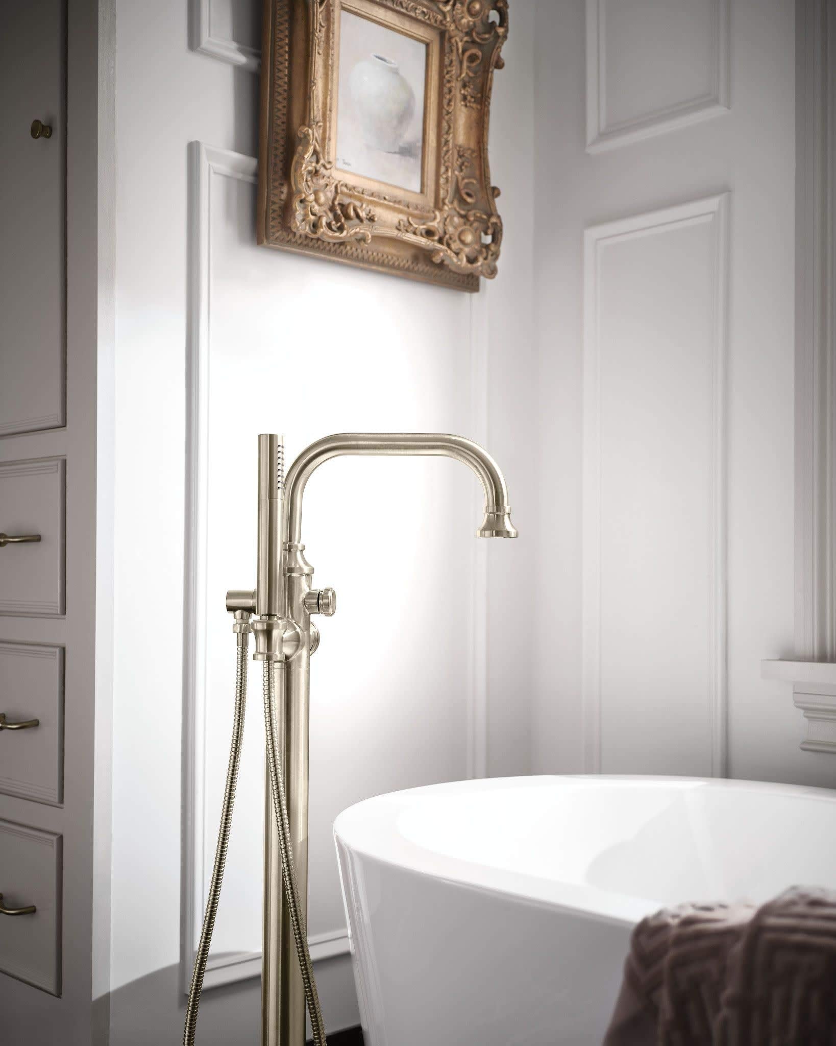 Brushed nickel freestanding tub filler with single handle, curved spout, and detachable handshower on hose.
