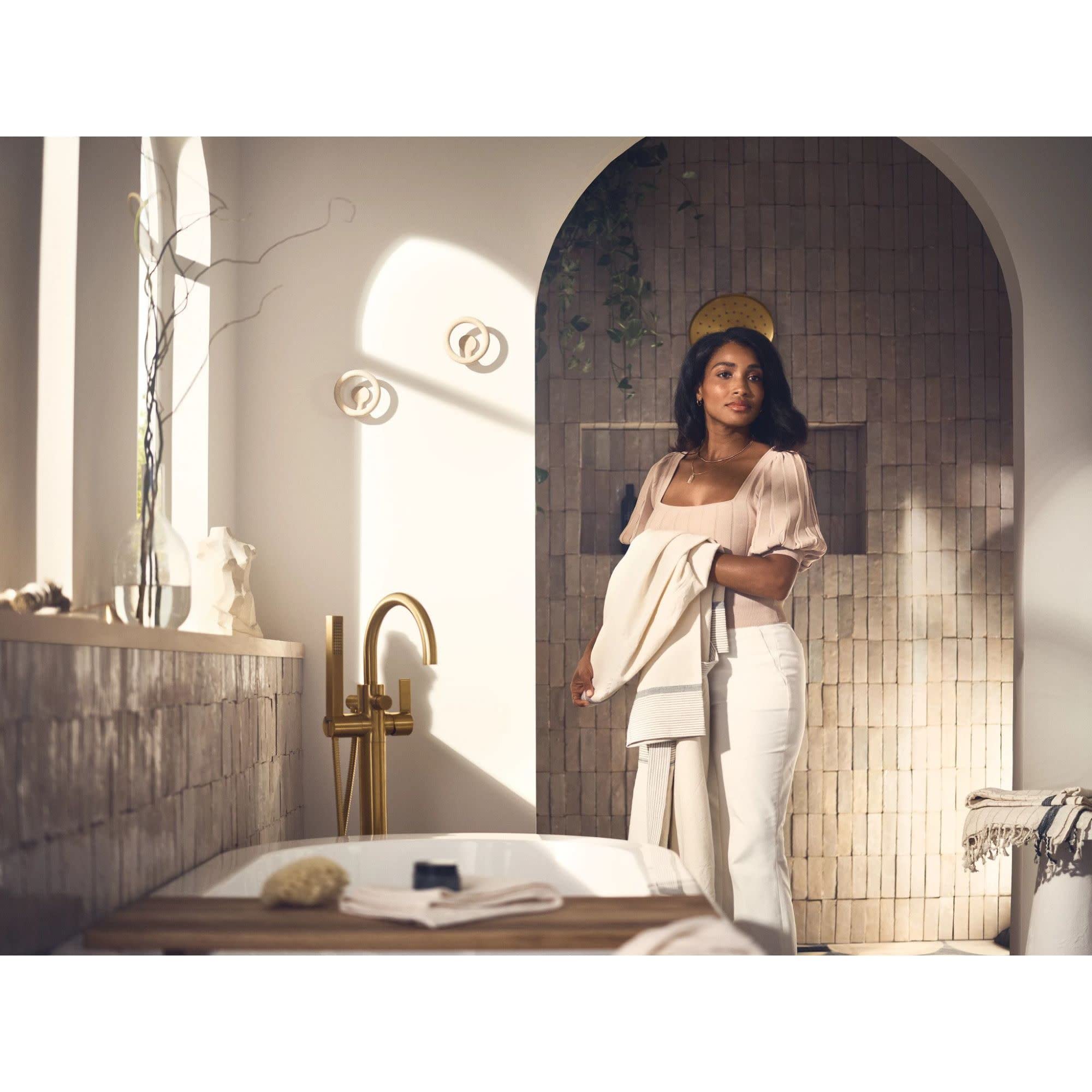 Brushed nickel freestanding tub filler with single handle and detachable handshower installed beside white bathtub.