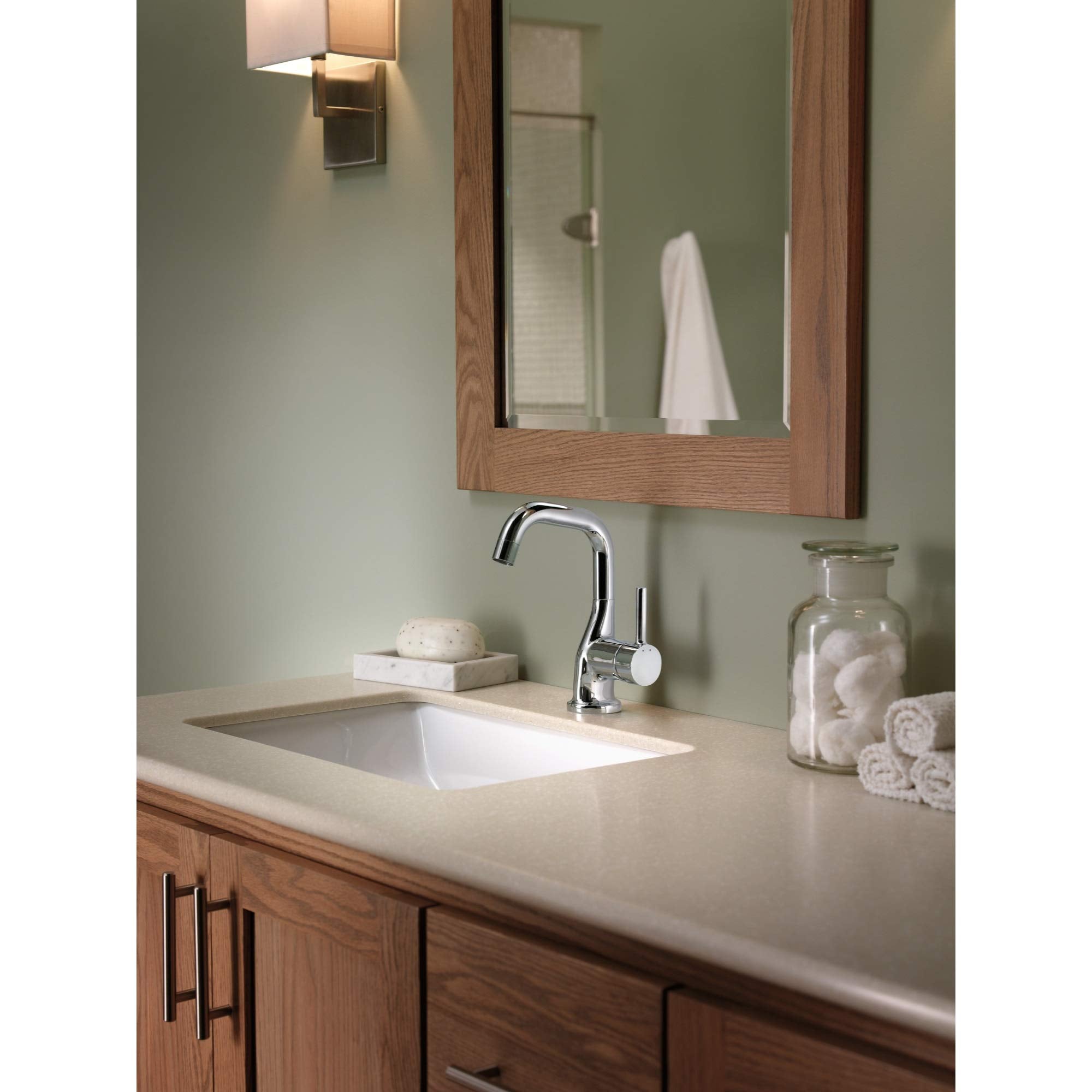 Chrome robe hook mounted on green bathroom wall beside mirror and sink.