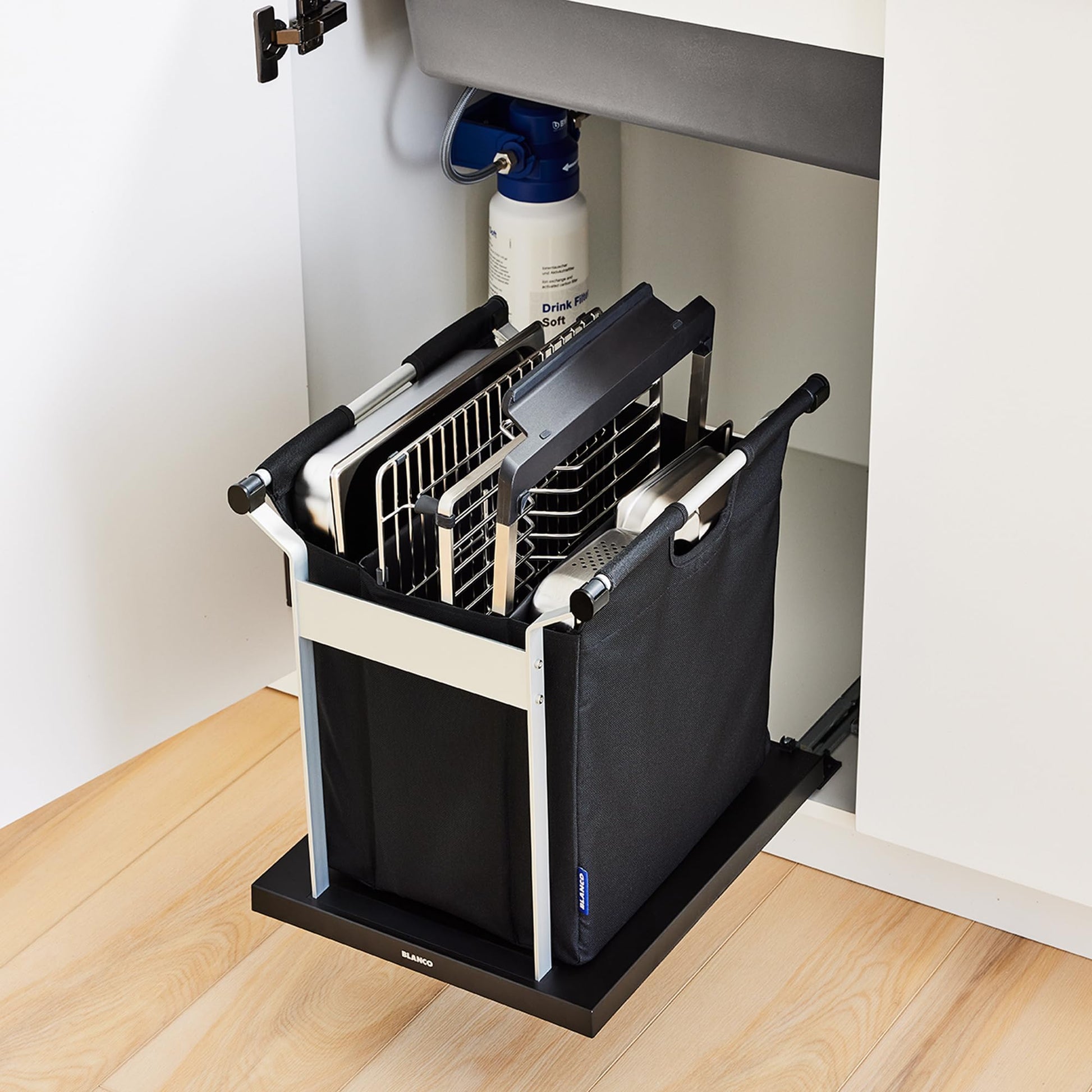 Black and white pull-out sink organizer with multiple compartments holding cutting boards and kitchen utensils under a sink c