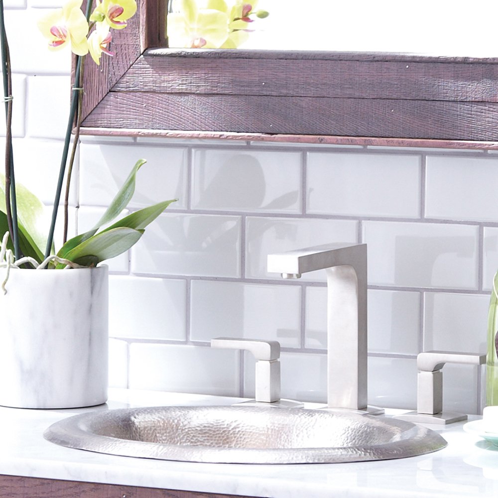 Brushed nickel bathroom sink with lotus-shaped hammered basin and matching tall faucet with side handles on white countertop.