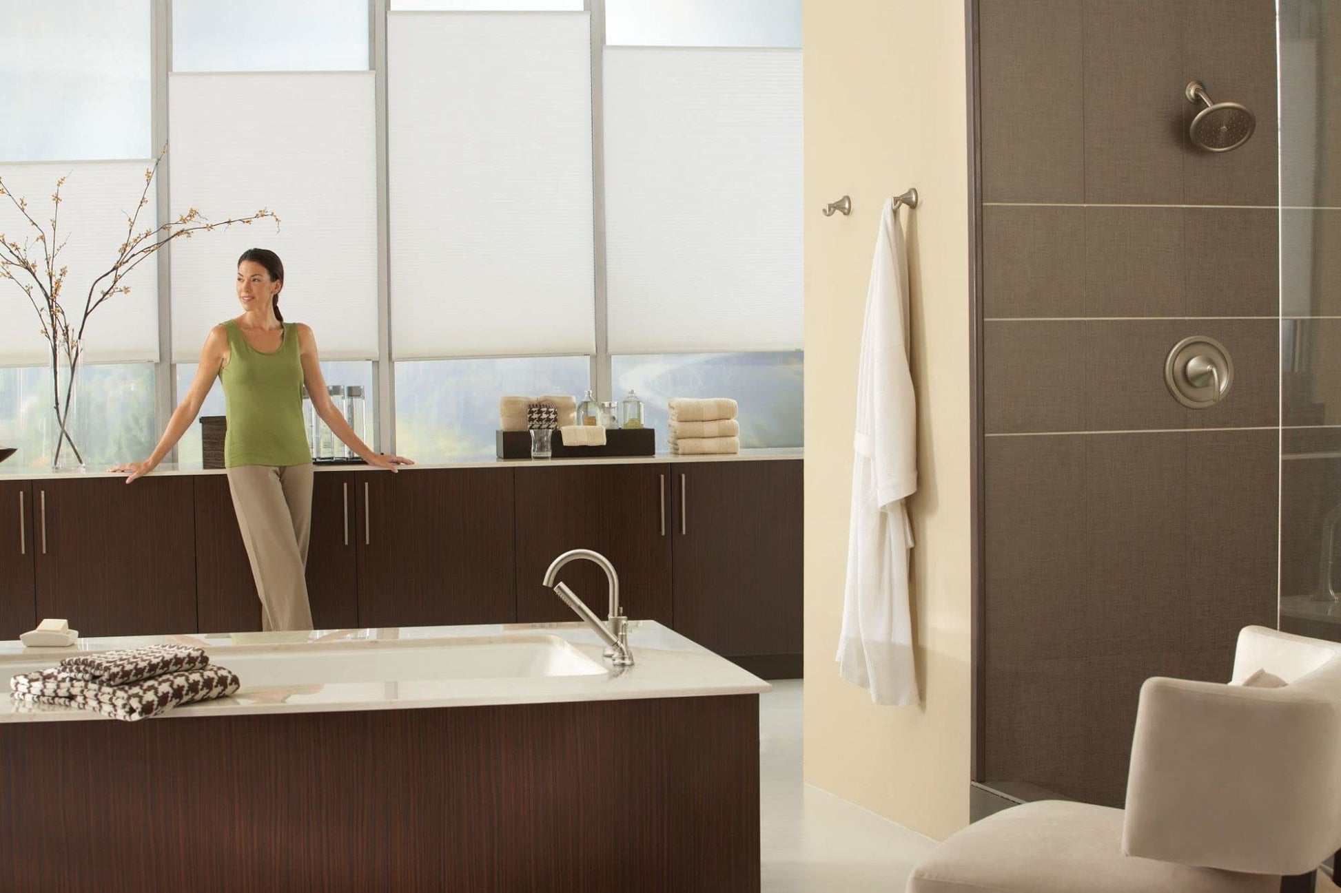 Brushed nickel circular showerhead mounted on brown tile wall with control valve below.