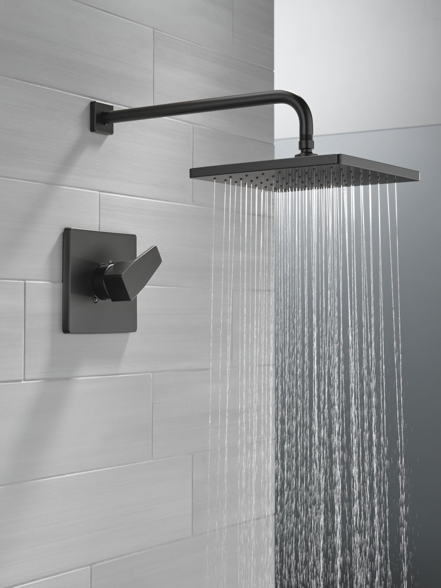Matte black shower trim with square showerhead, curved arm, and lever handle mounted on white subway tile wall.