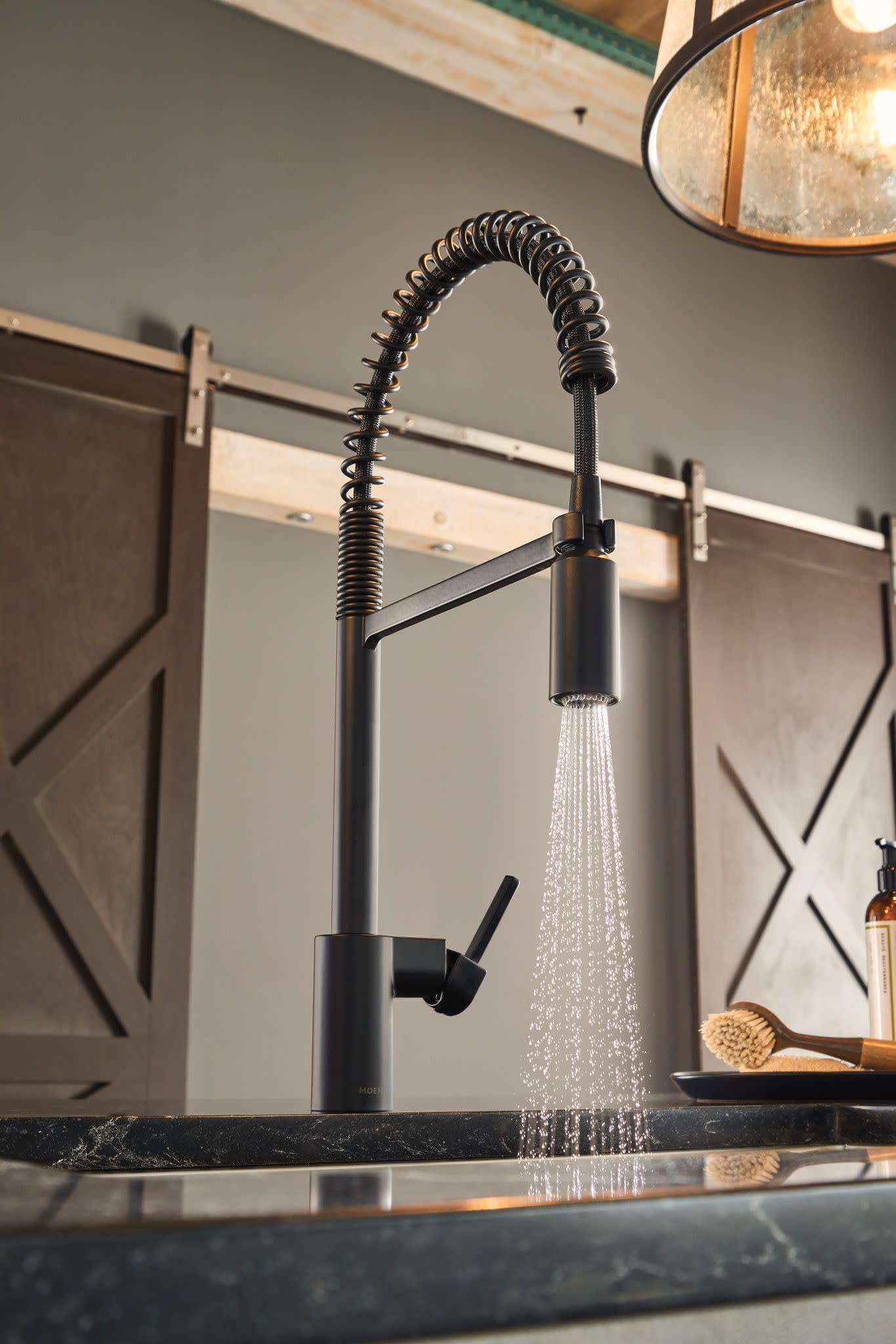Matte black pulldown kitchen faucet with coiled hose and sprayer head mounted on dark countertop.