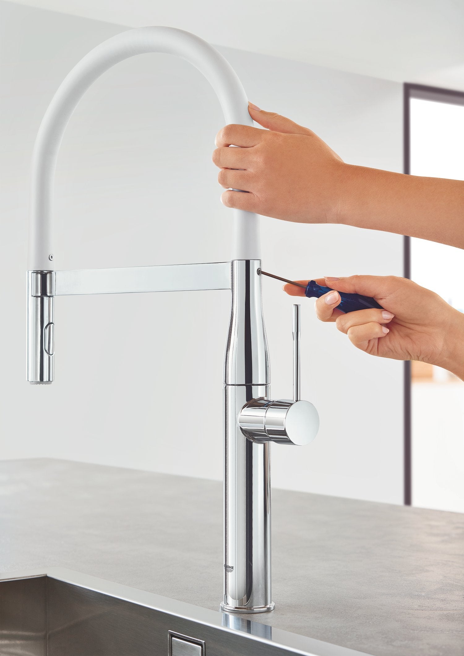 Chrome kitchen faucet with white flexible hose and pull-down sprayer, demonstrated with hands showing spray function.