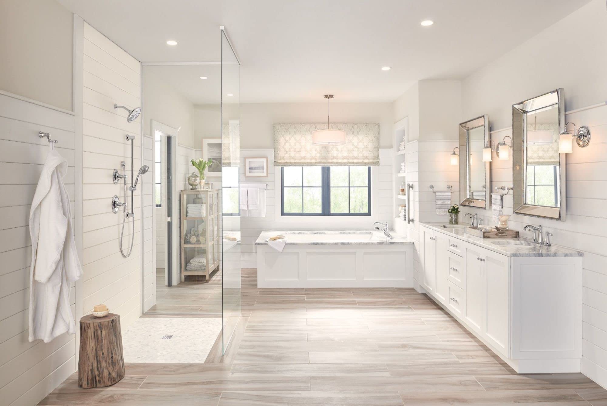 Chrome two-handle deck-mounted roman tub faucet with hand shower mounted on white bathtub rim.