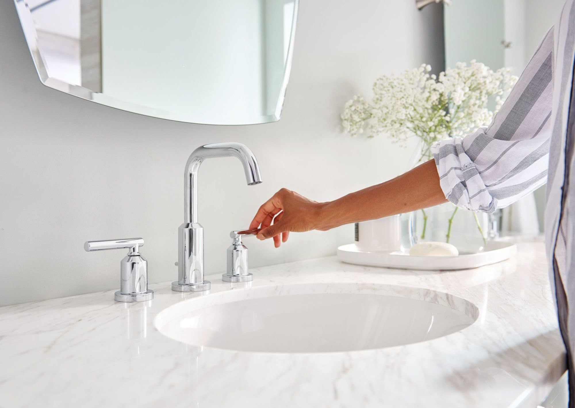 Chrome two-handle bathroom sink faucet with high arc spout installed on marble countertop with round basin.