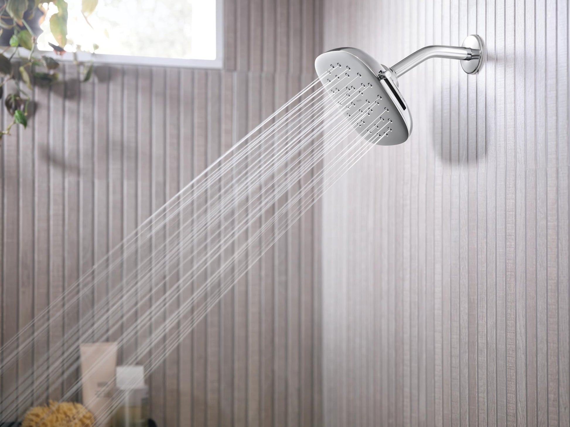Chrome square rain shower head mounted on wall with water spray visible and curved arm extending from ceiling mount.