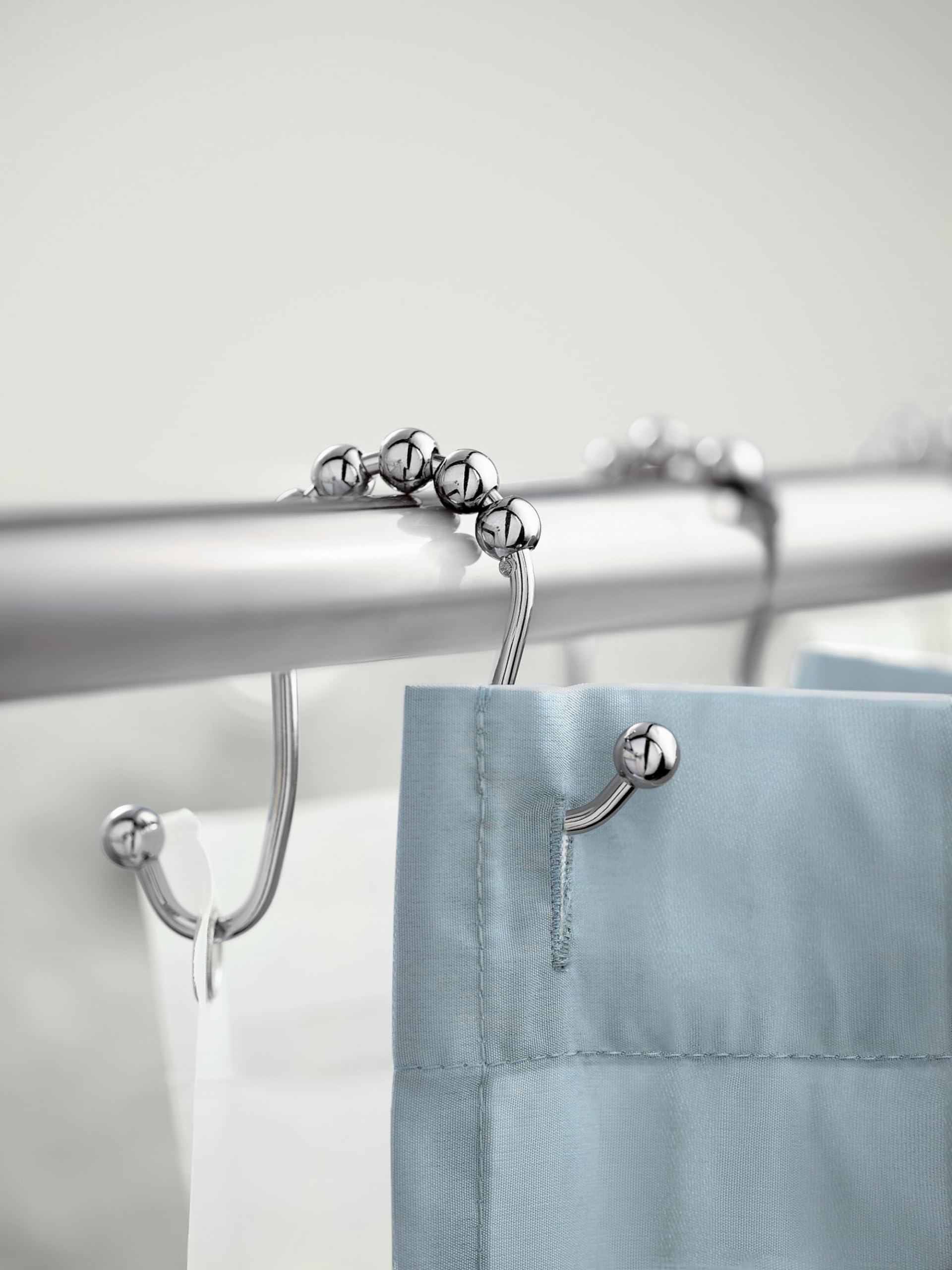 Chrome curved shower curtain rod with ball-shaped rings holding blue and white fabric curtains.