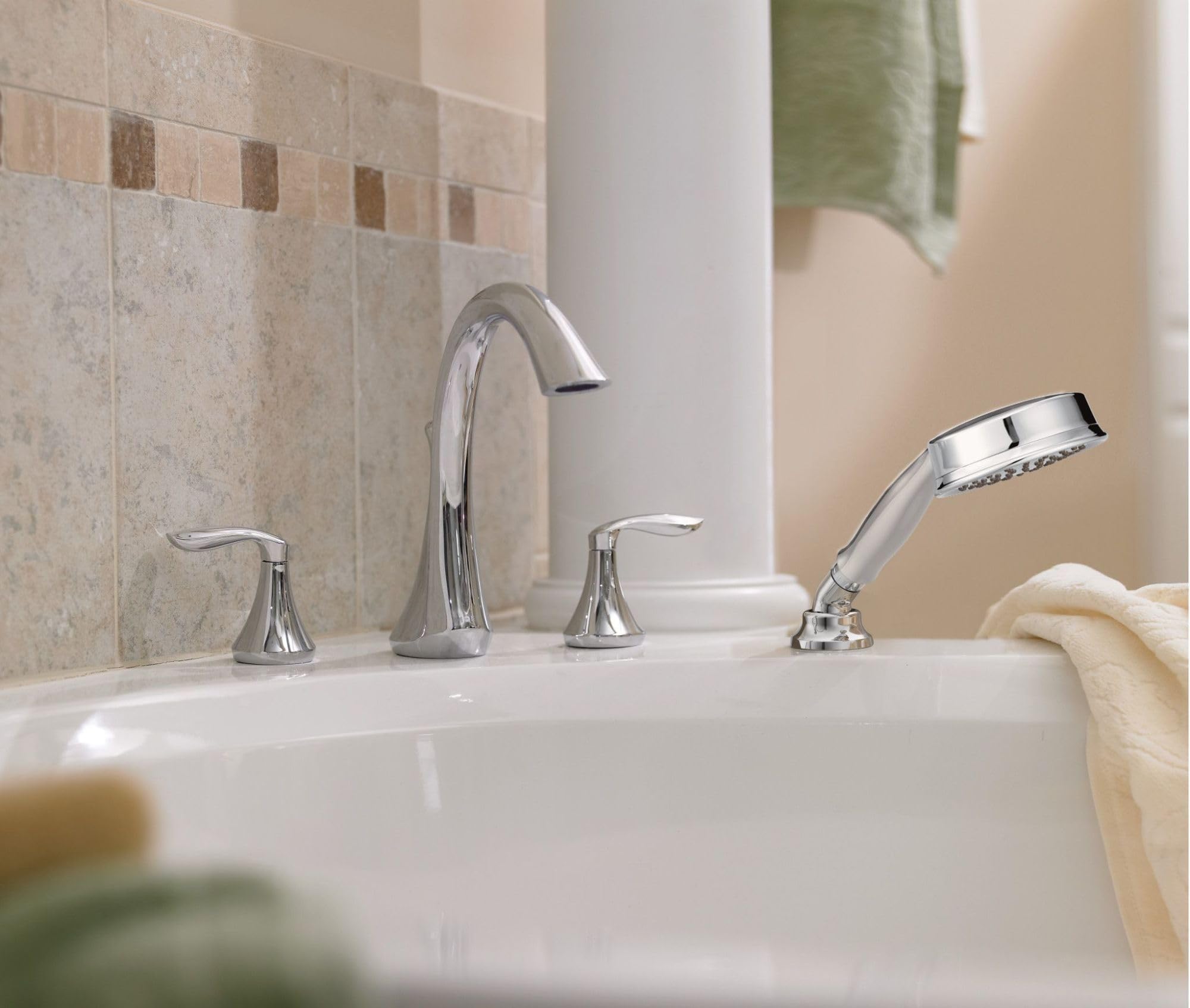 Chrome two-handle roman tub faucet with curved spout and detachable handheld showerhead mounted on white bathtub deck.