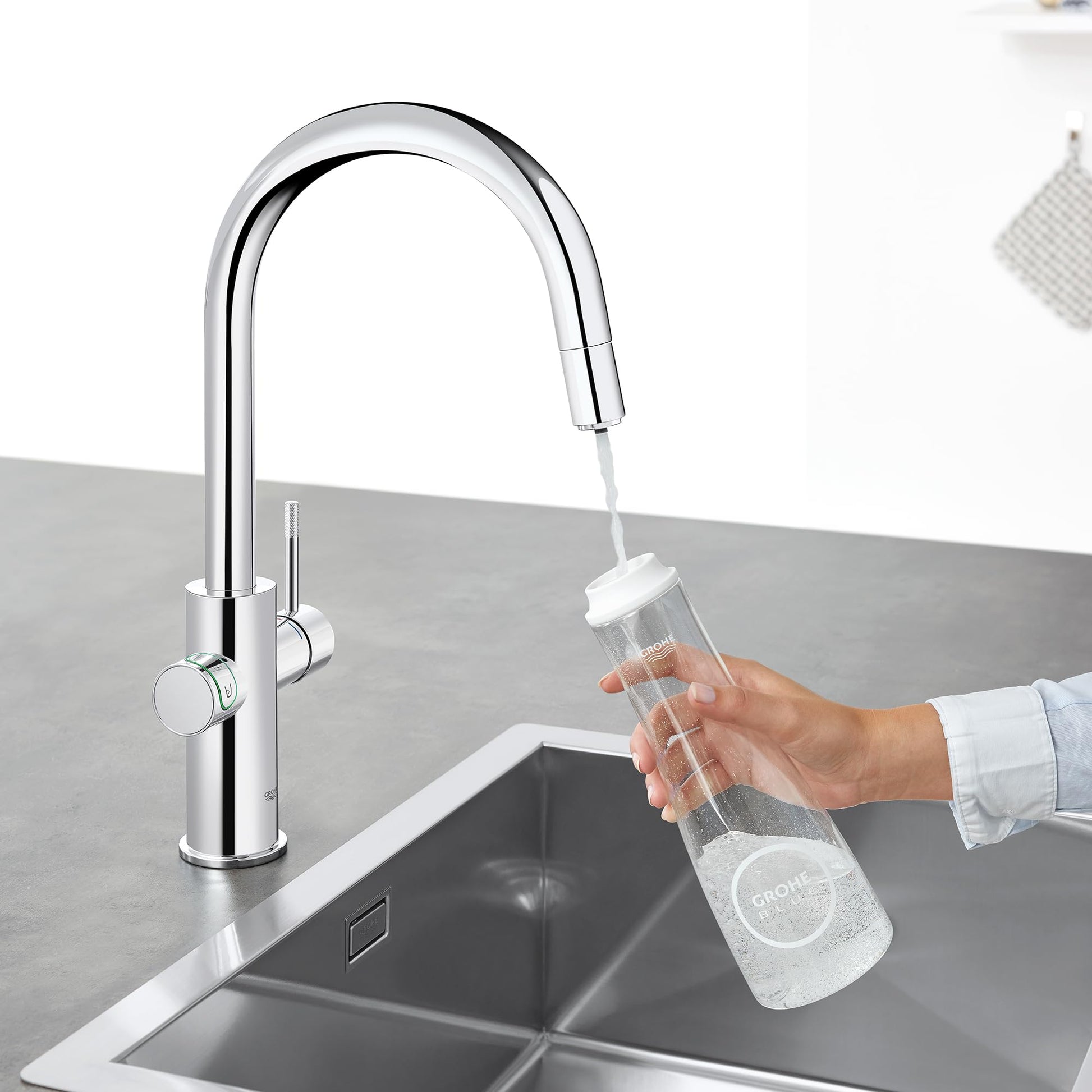 Chrome pull-down kitchen faucet with curved spout and single handle, dispensing water into a clear bottle.