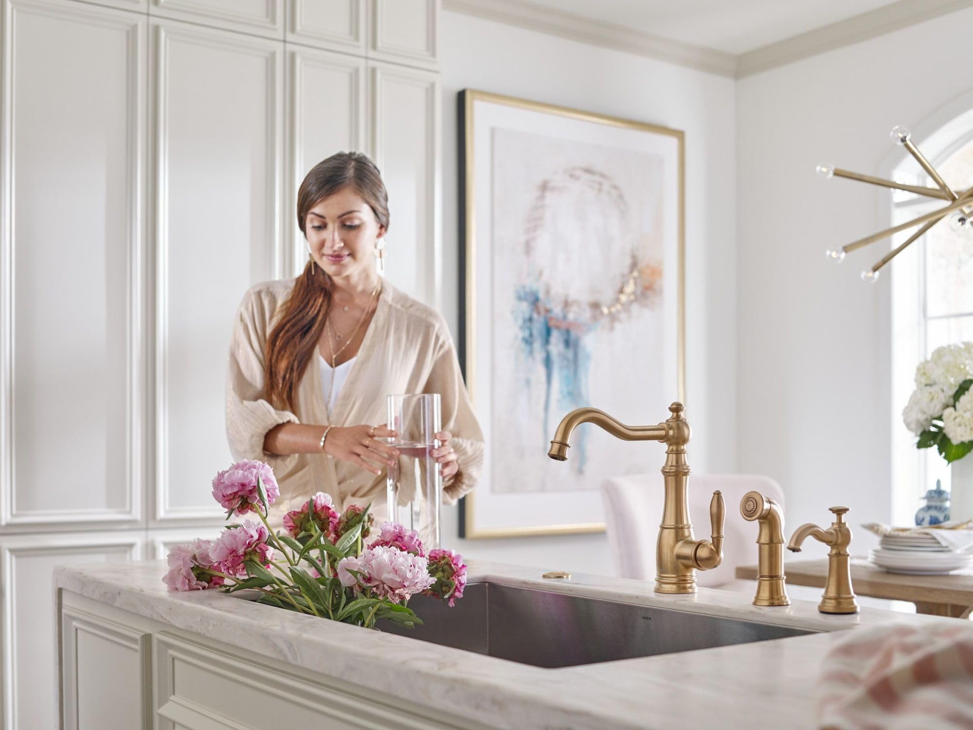 Brushed gold deck-mounted kitchen soap dispenser with curved spout installed above sink next to matching faucet.