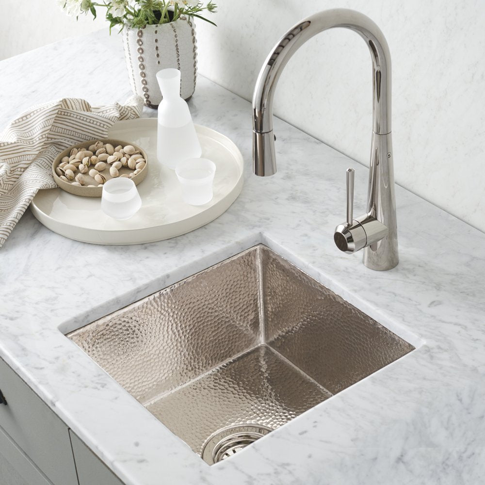 Polished nickel dual-compartment bar sink with hammered finish and matching pull-down faucet on marble countertop.