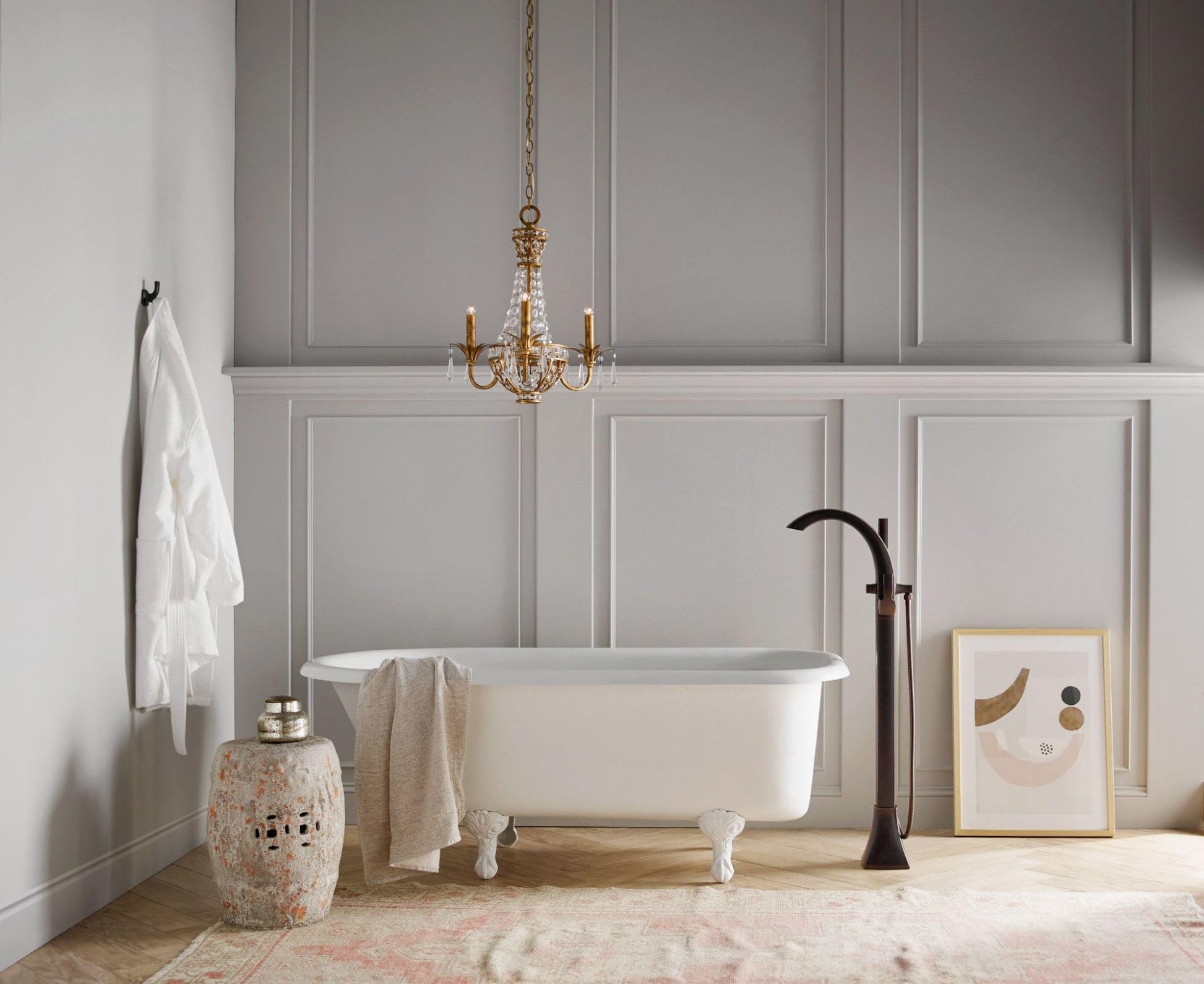 Oil rubbed bronze freestanding tub filler with single handle and attached handshower next to white soaking tub.