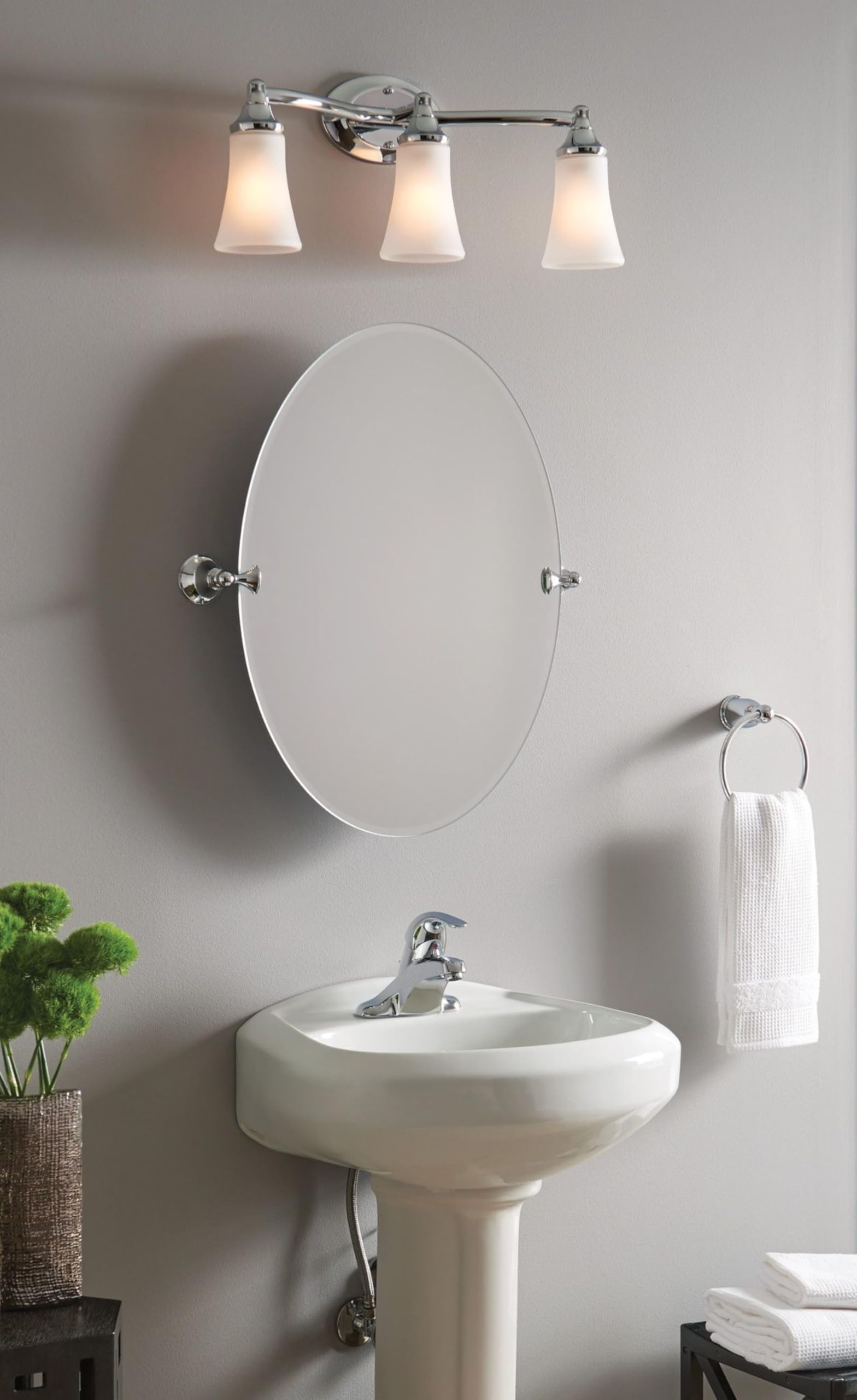 Chrome vanity fixture with three frosted glass shades mounted above a bathroom sink and oval mirror.