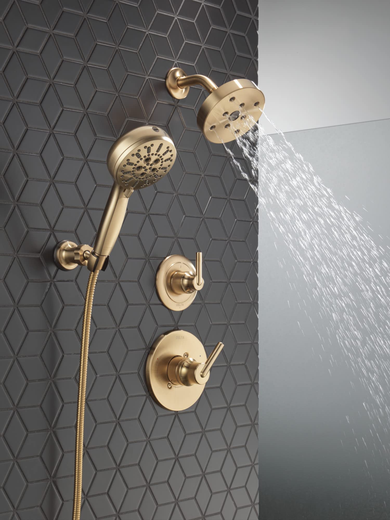 Champagne bronze wall-mounted shower system with fixed showerhead, handheld spray, and control valves spraying water against 