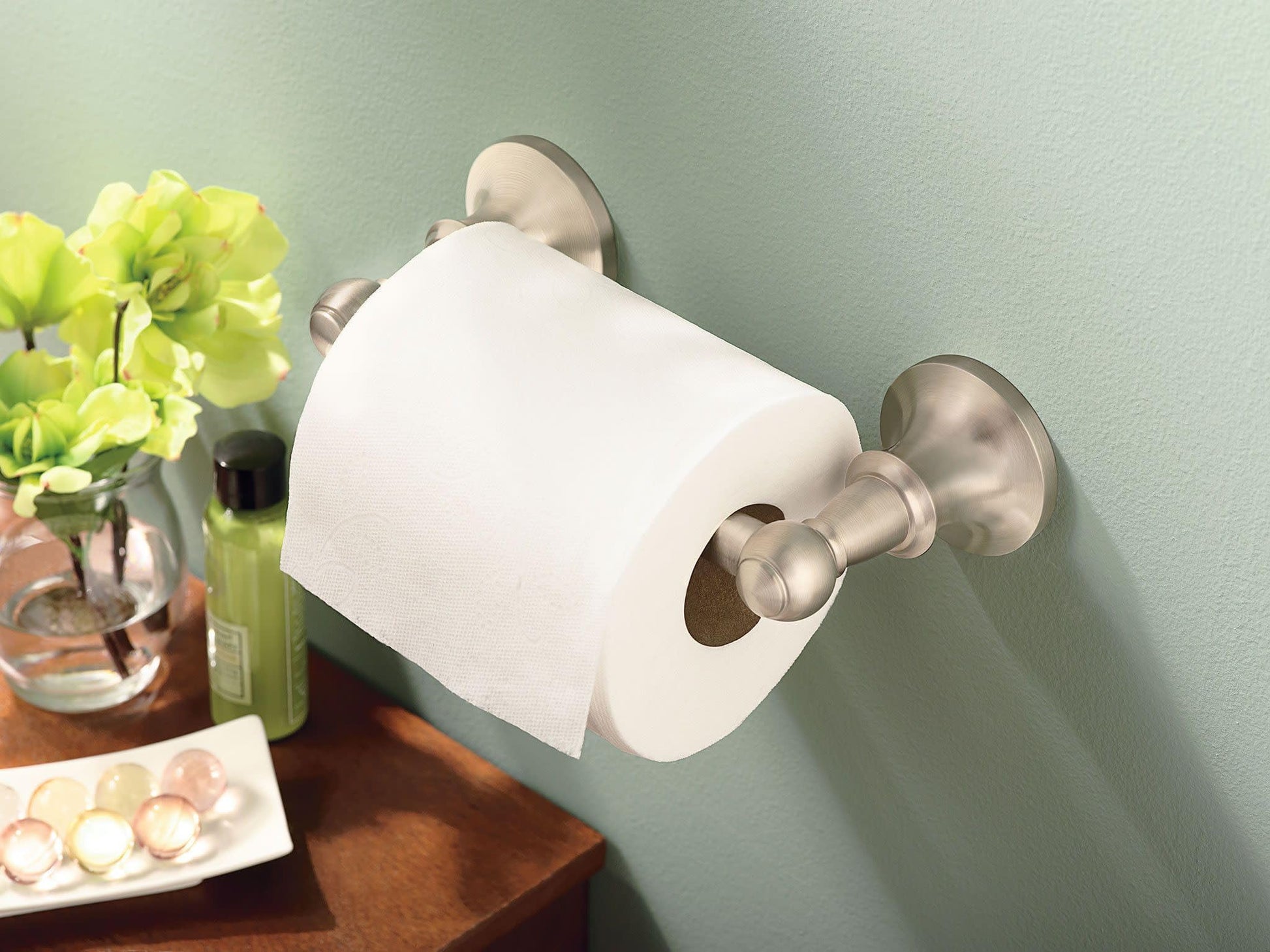 Brushed nickel pivoting toilet paper holder mounted on wall with white roll installed.