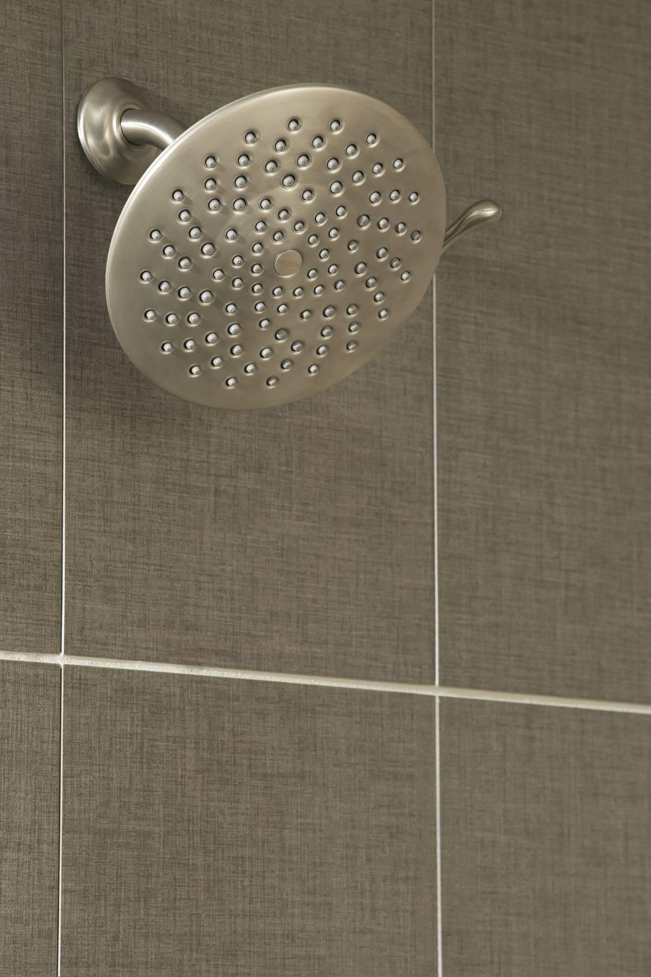 Brushed gold round showerhead with multiple spray holes mounted on wall with adjustment arm.