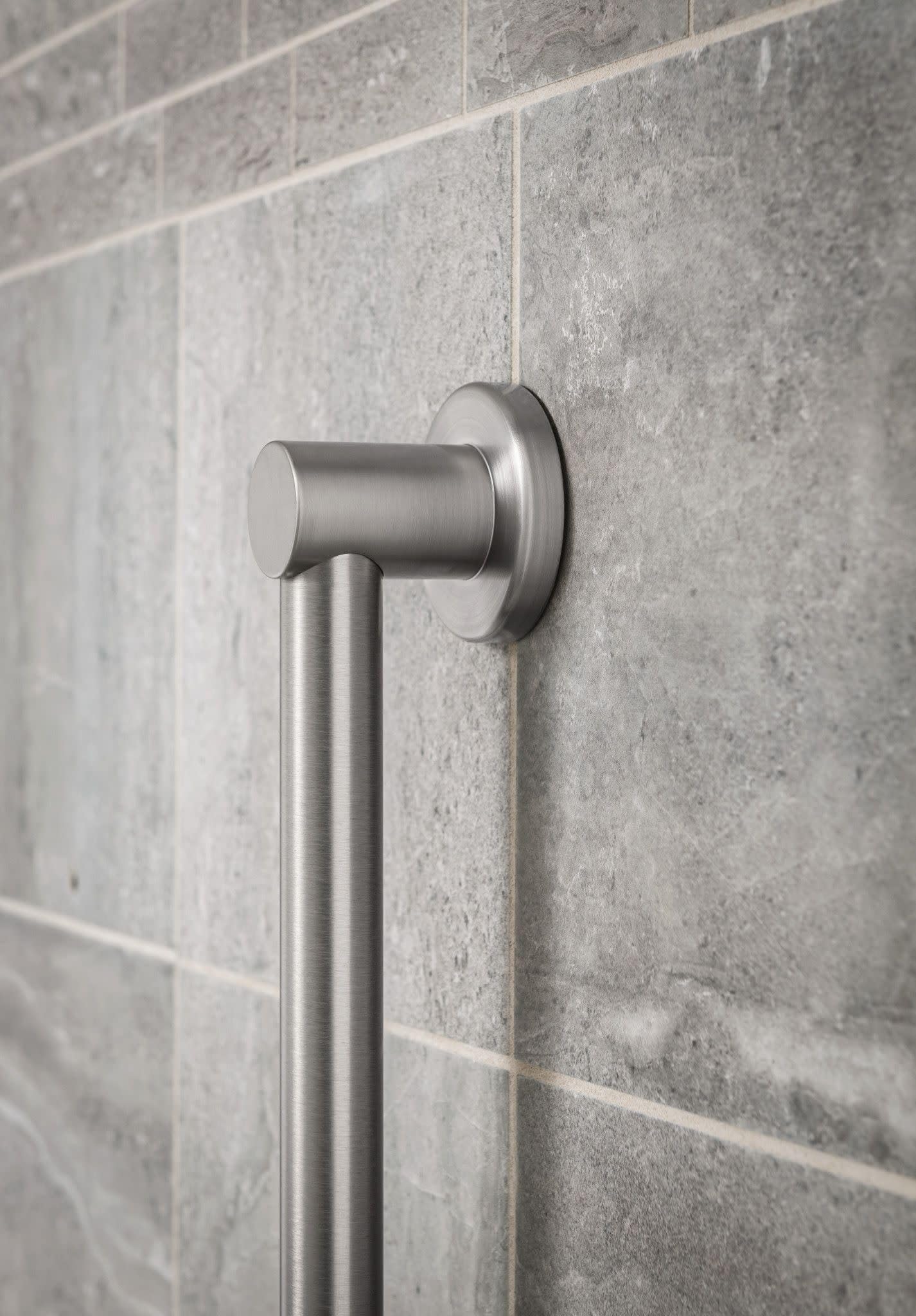 Brushed nickel stainless steel grab bar mounted horizontally on gray tile bathroom wall.