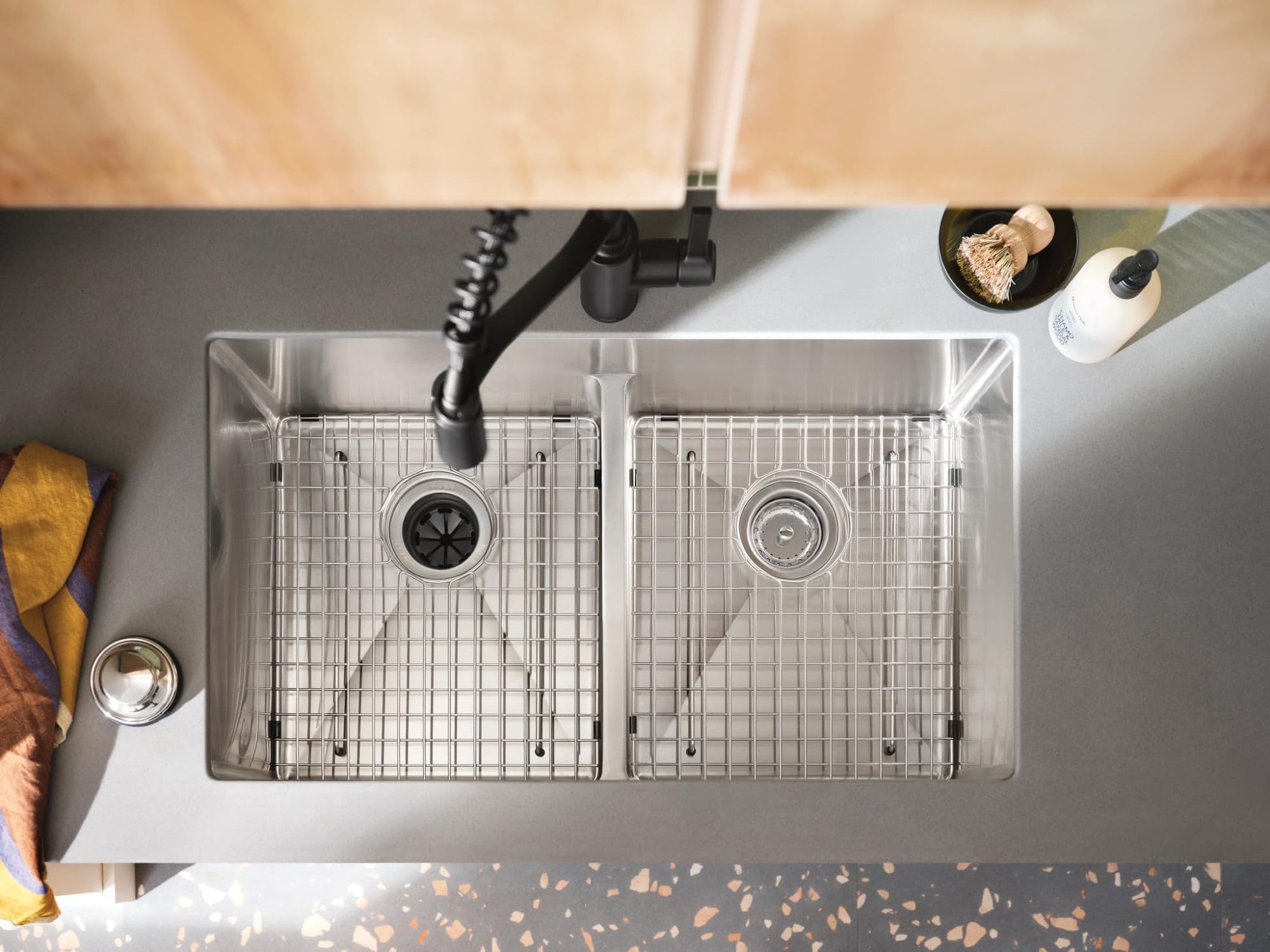 Stainless steel double bowl kitchen sink with low divider, bottom grids, and black faucet installed in countertop.