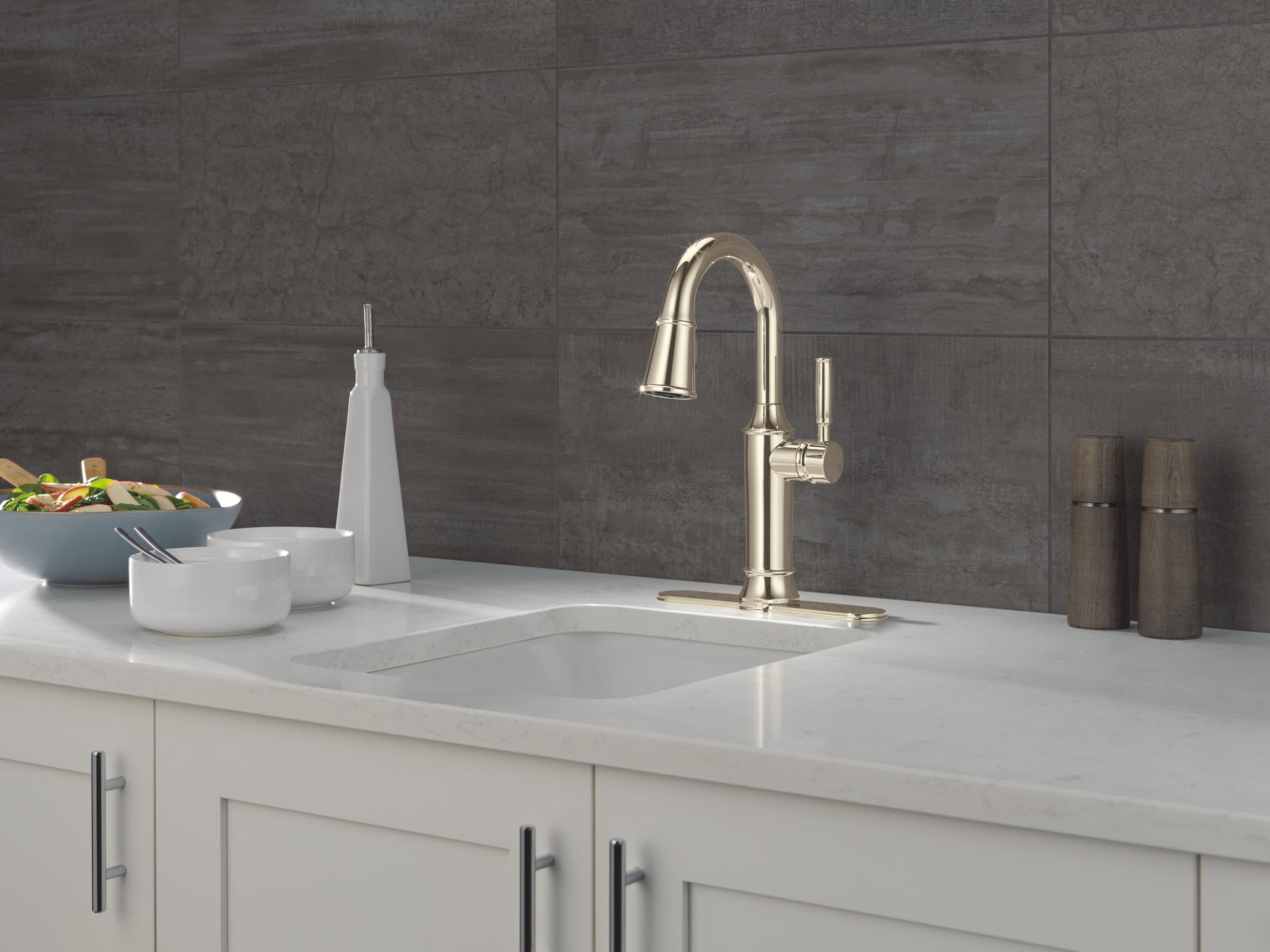 Polished stainless steel pulldown kitchen faucet with curved spout mounted on white countertop sink.