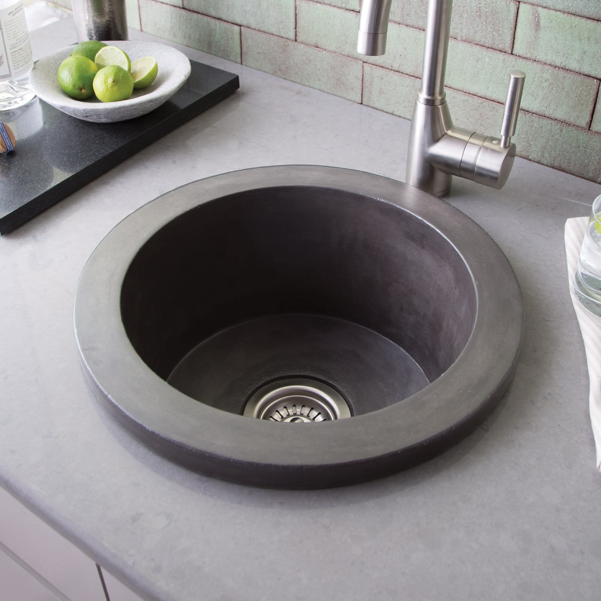 Slate-colored round prep sink with wide rim and drain, installed in light countertop with stainless steel faucet and green ti