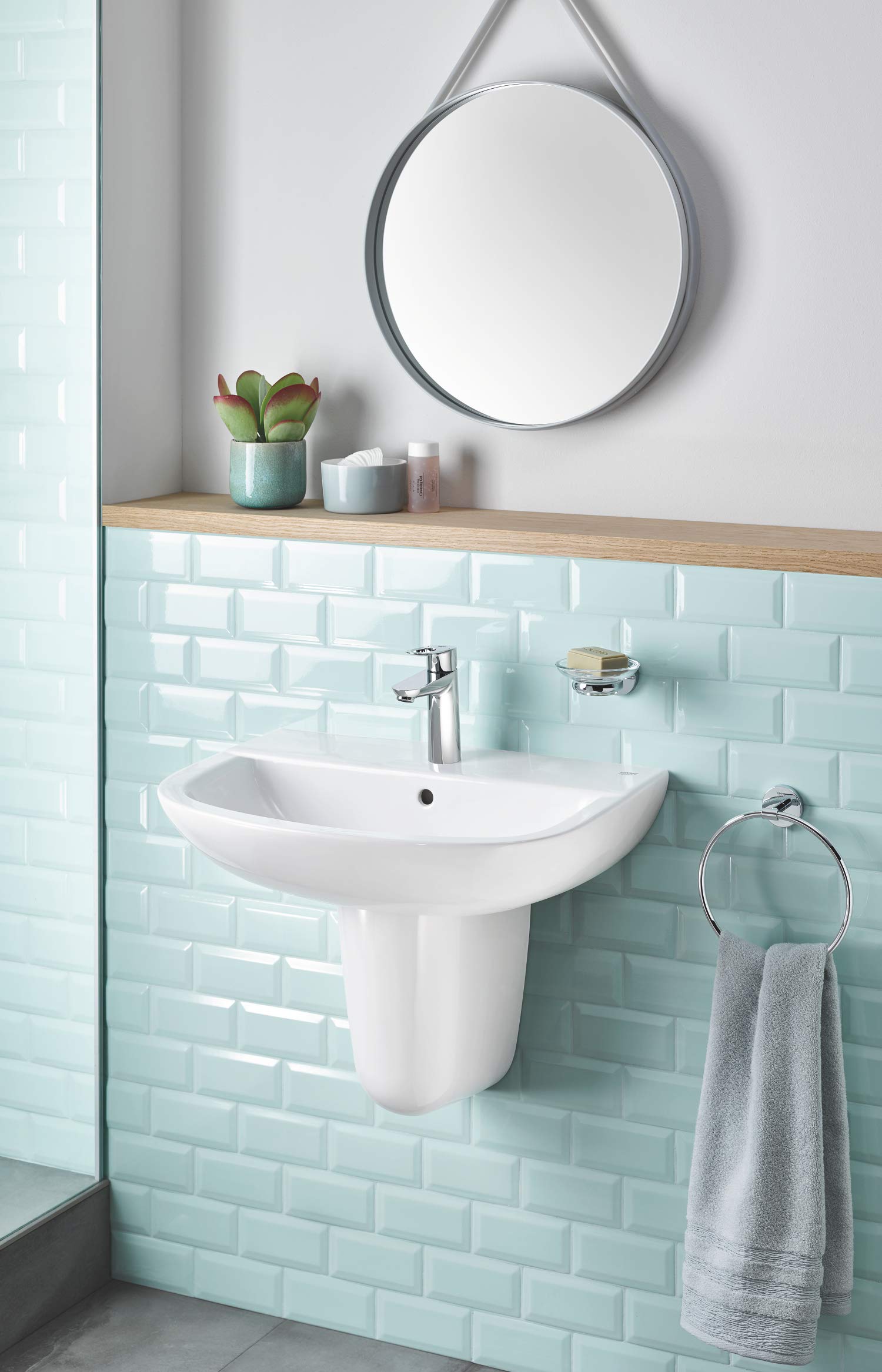 Chrome towel ring with curved design mounted on bathroom wall beside sink with folded towel hanging from it.