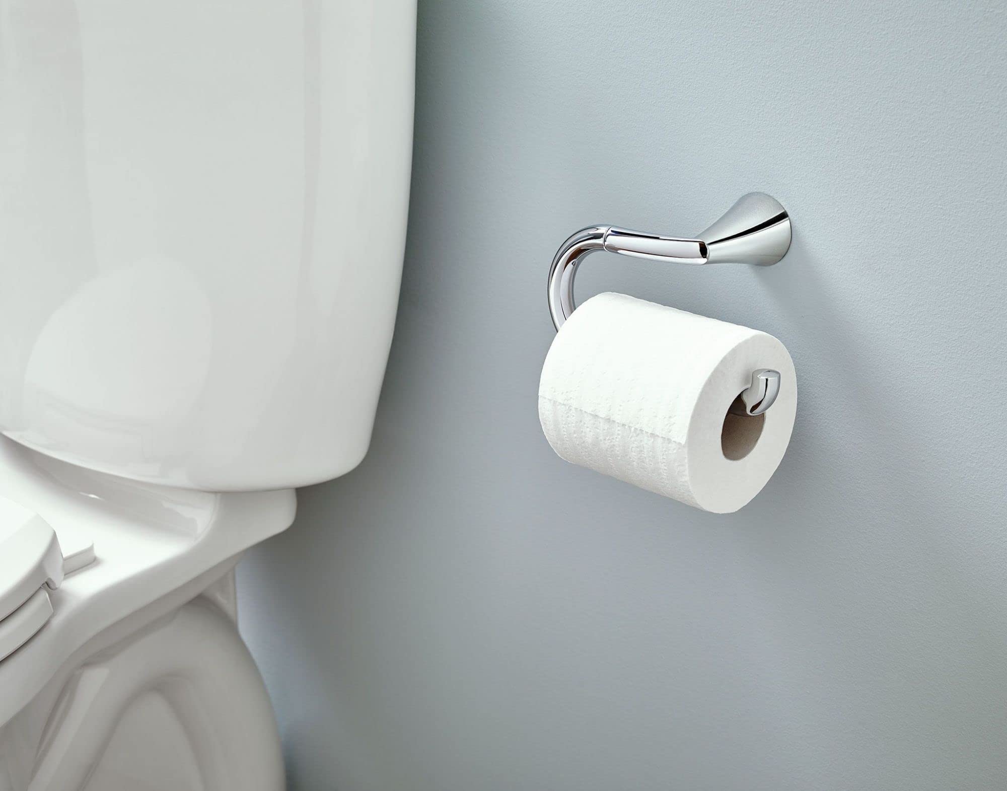 Chrome toilet paper holder mounted on gray bathroom wall with white toilet paper roll installed.