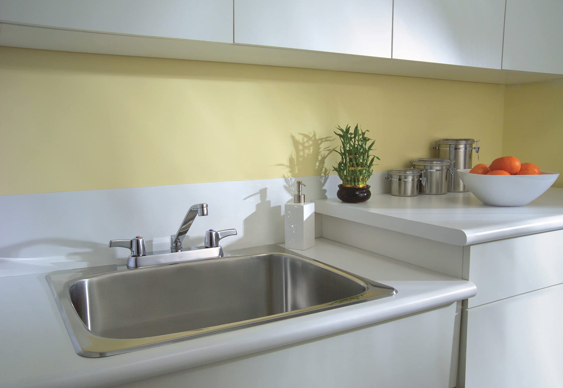 Chrome two-handle deck mount faucet with 8-inch spread installed on white countertop above stainless steel sink.