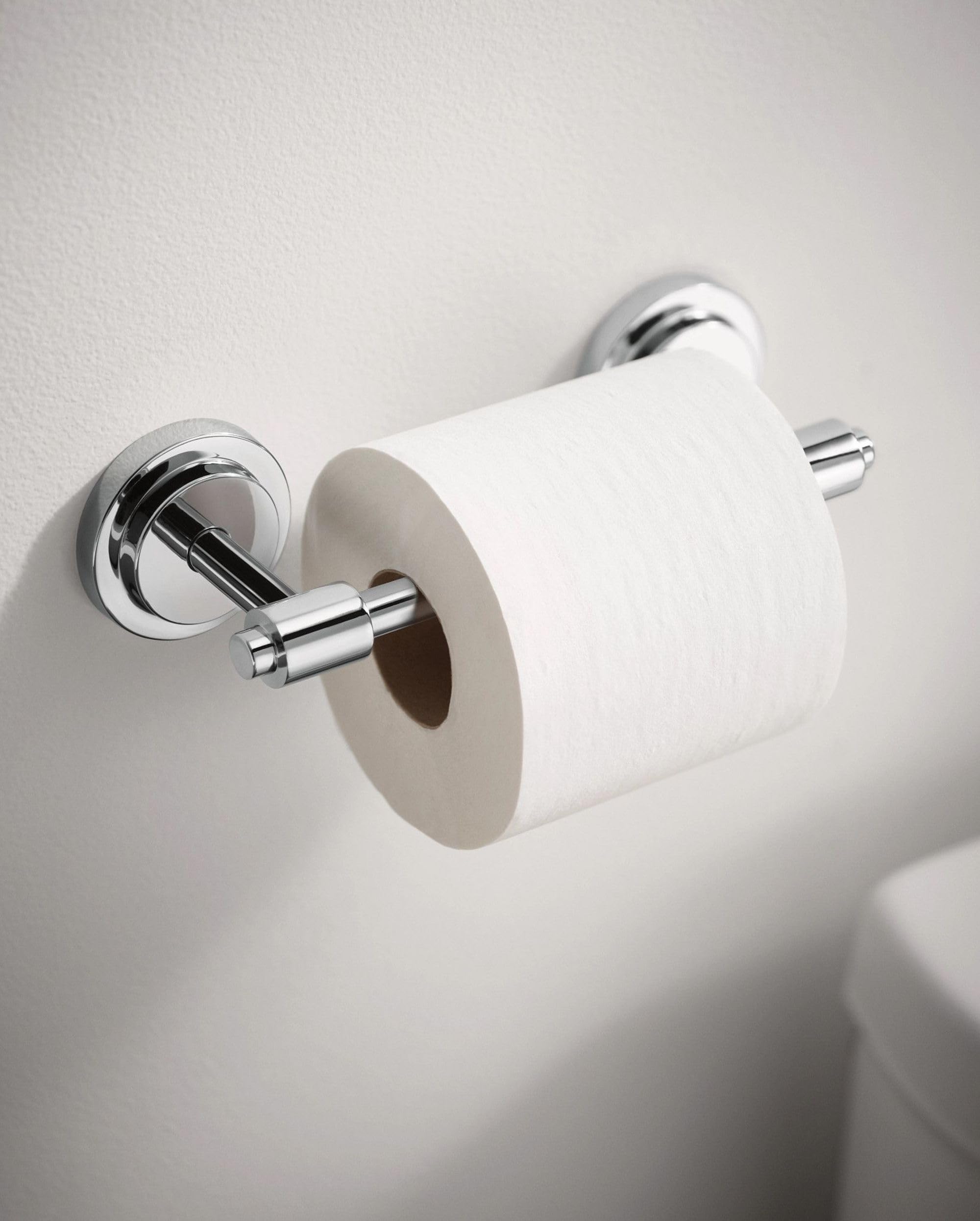 Chrome toilet paper holder mounted on white wall with white roll installed and pivoting arm extended to the right.