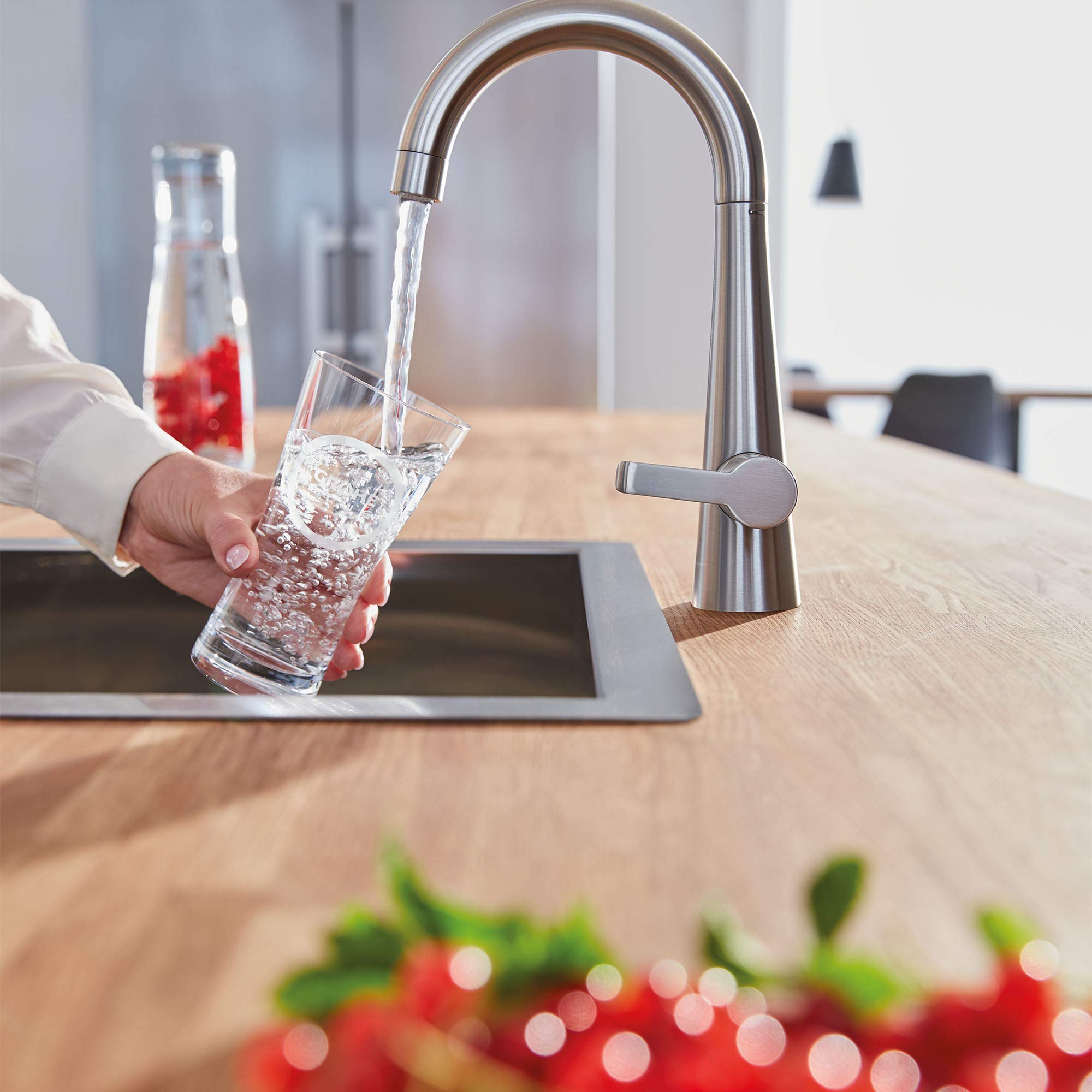 Stainless steel single-handle beverage faucet with arched spout dispensing filtered water into a glass over a kitchen counter