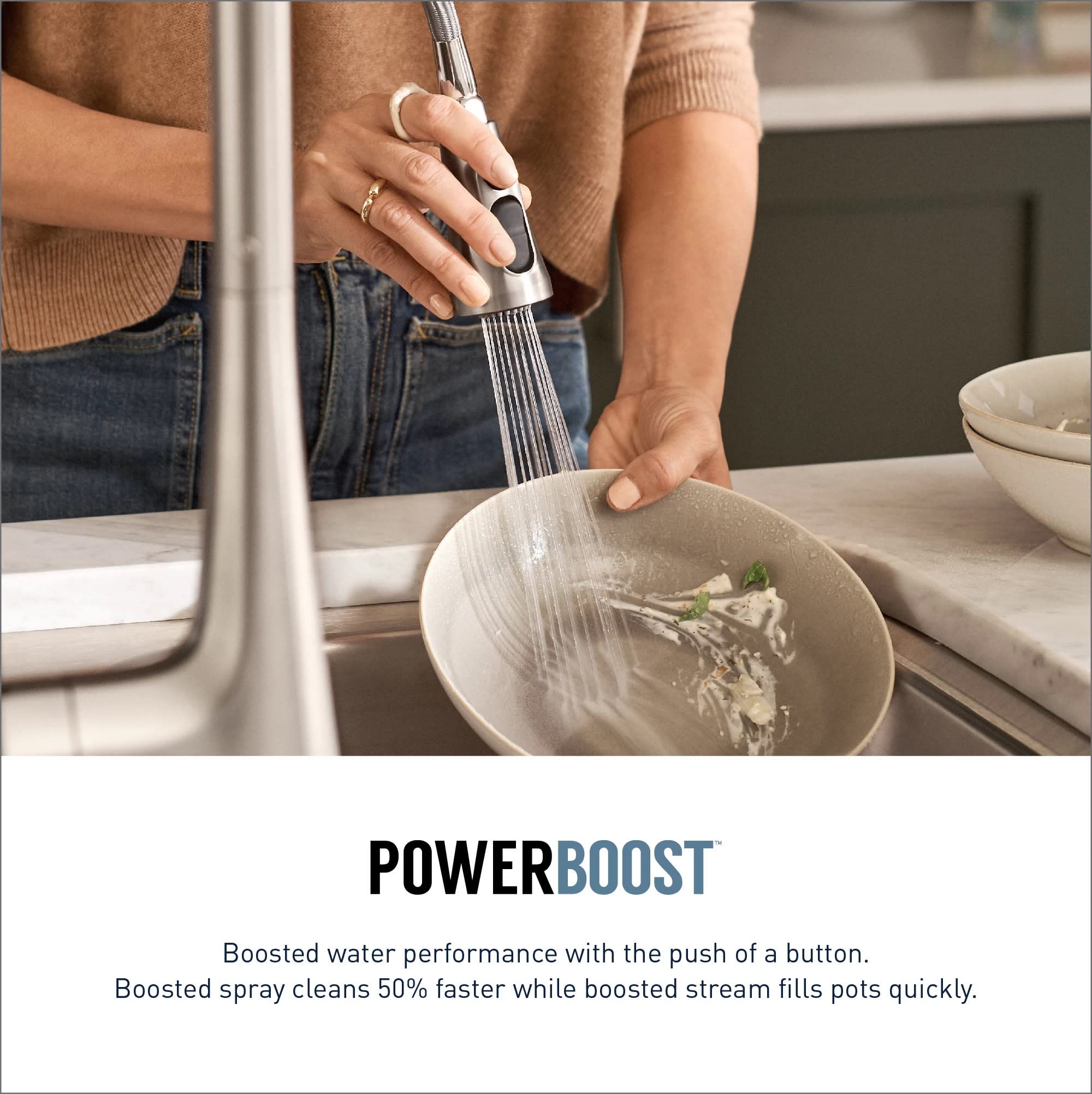 Matte black pulldown kitchen faucet with spray head being used to rinse vegetables in a white bowl.